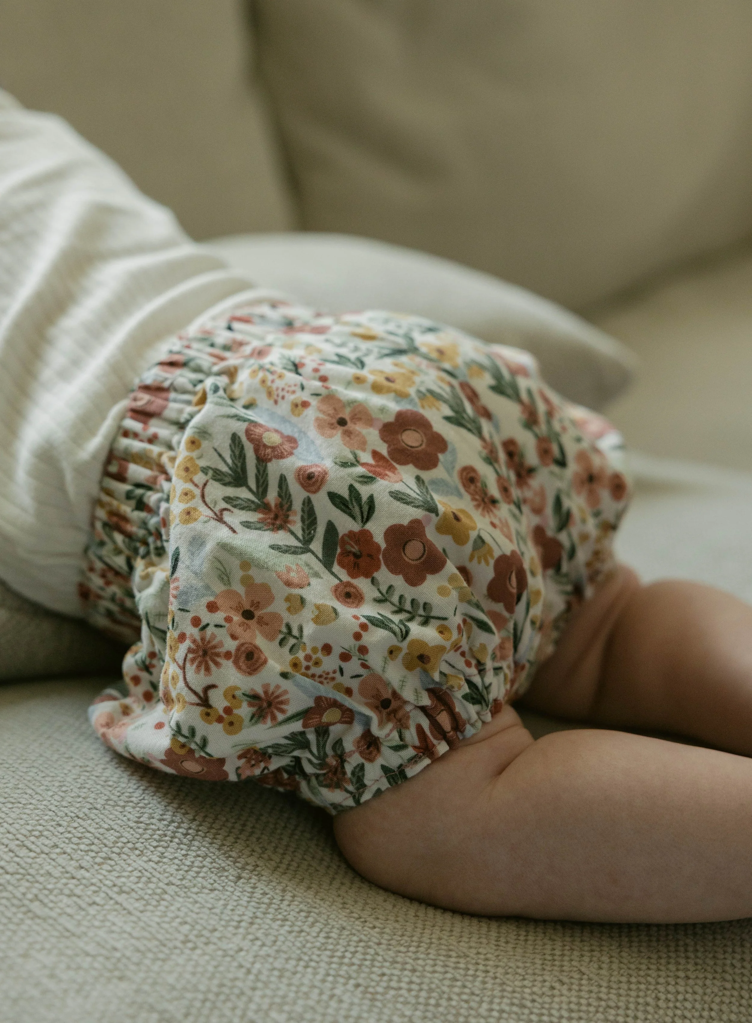 Close-up of a baby's bottom wearing floral-patterned diaper cover, lying on a textured beige surface.