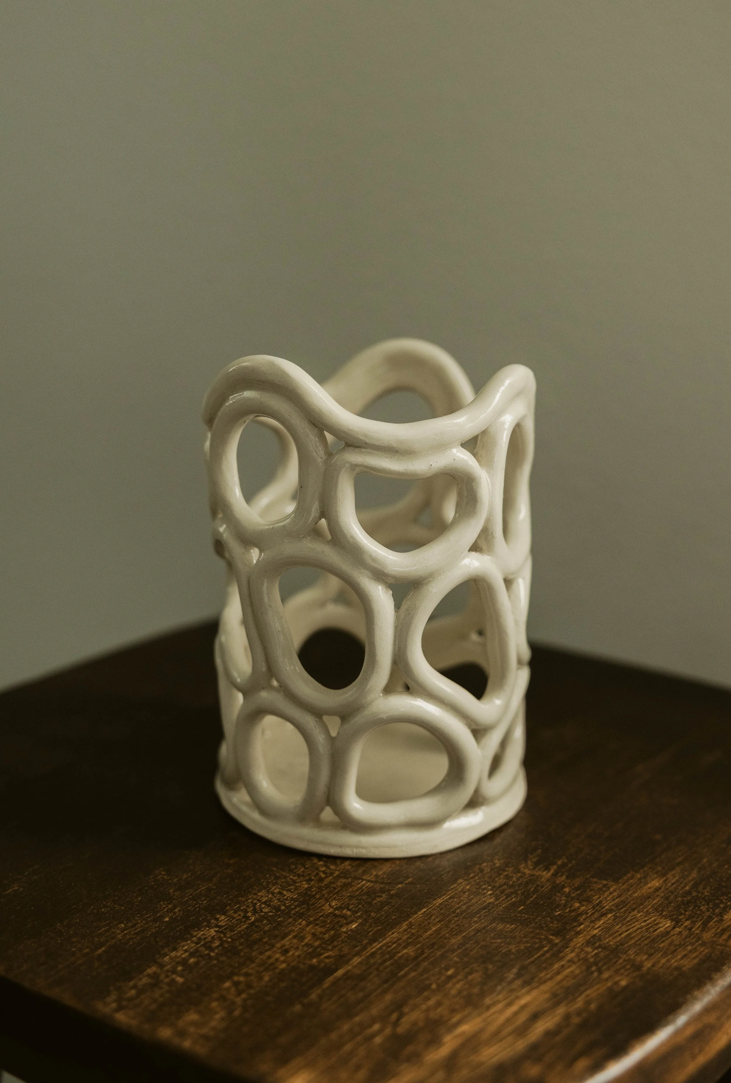 White decorative ceramic vase with an open, interconnected circular pattern, sitting on a dark wooden surface.