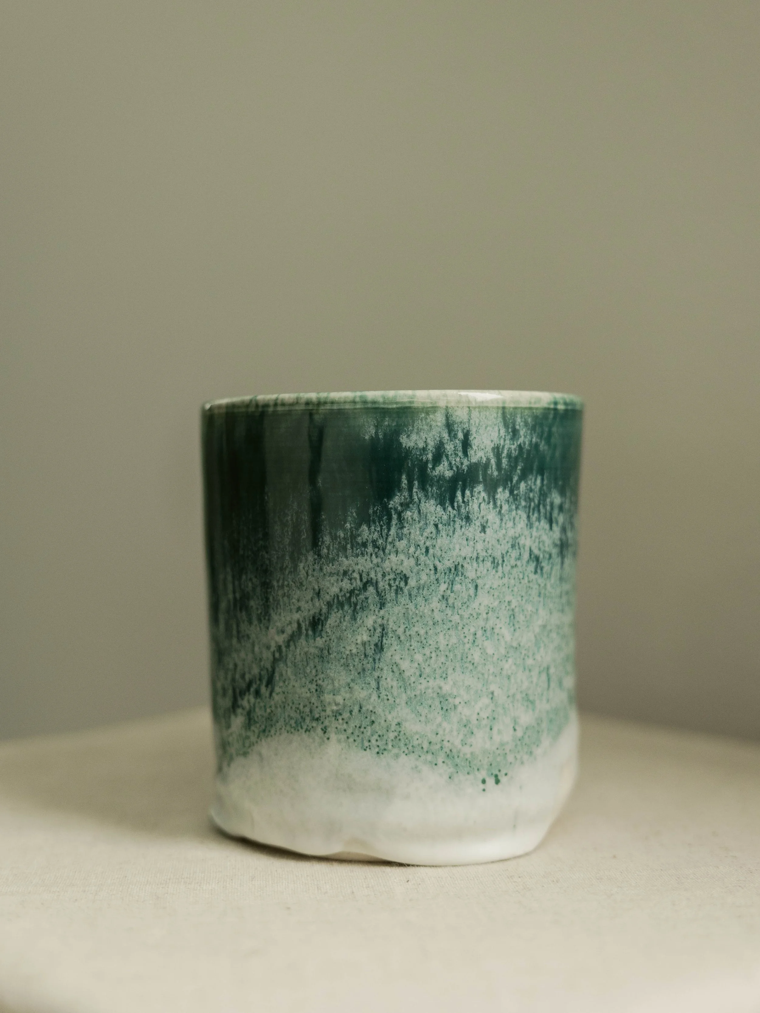 Ceramic cup with a textured green and black glaze, placed on a neutral surface against a plain background.