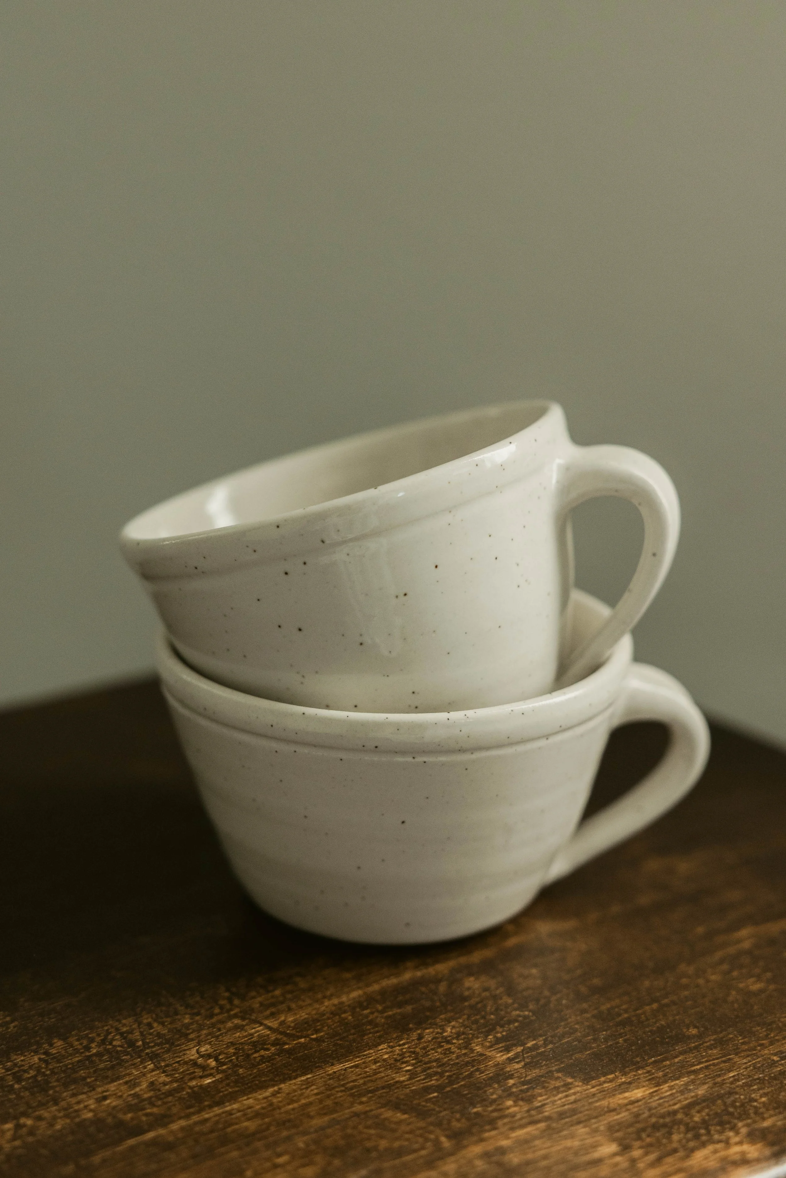 Stacked white ceramic cups with speckled glaze on a wooden surface.