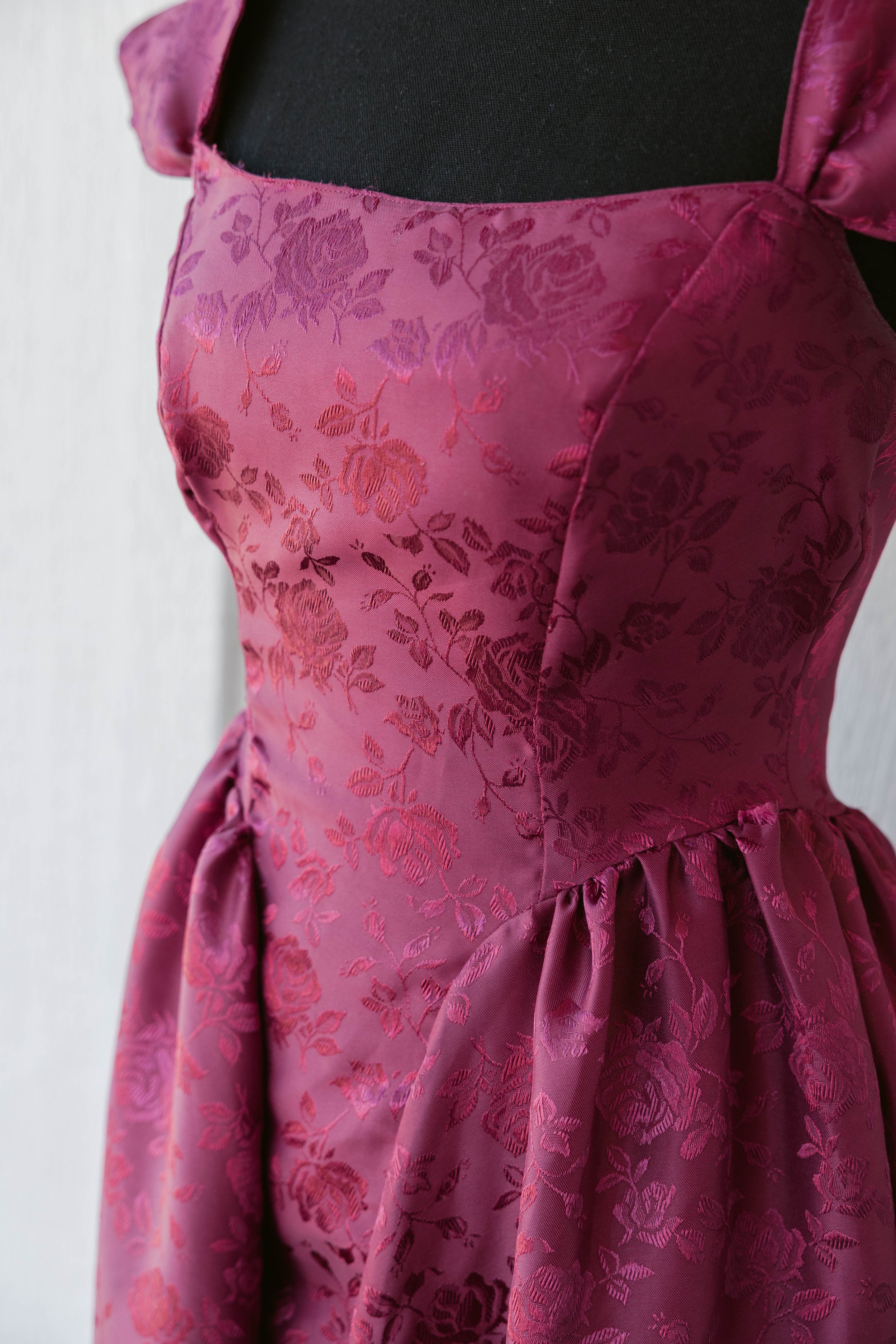 A pink satin dress with floral embroidery displayed on a black mannequin.
