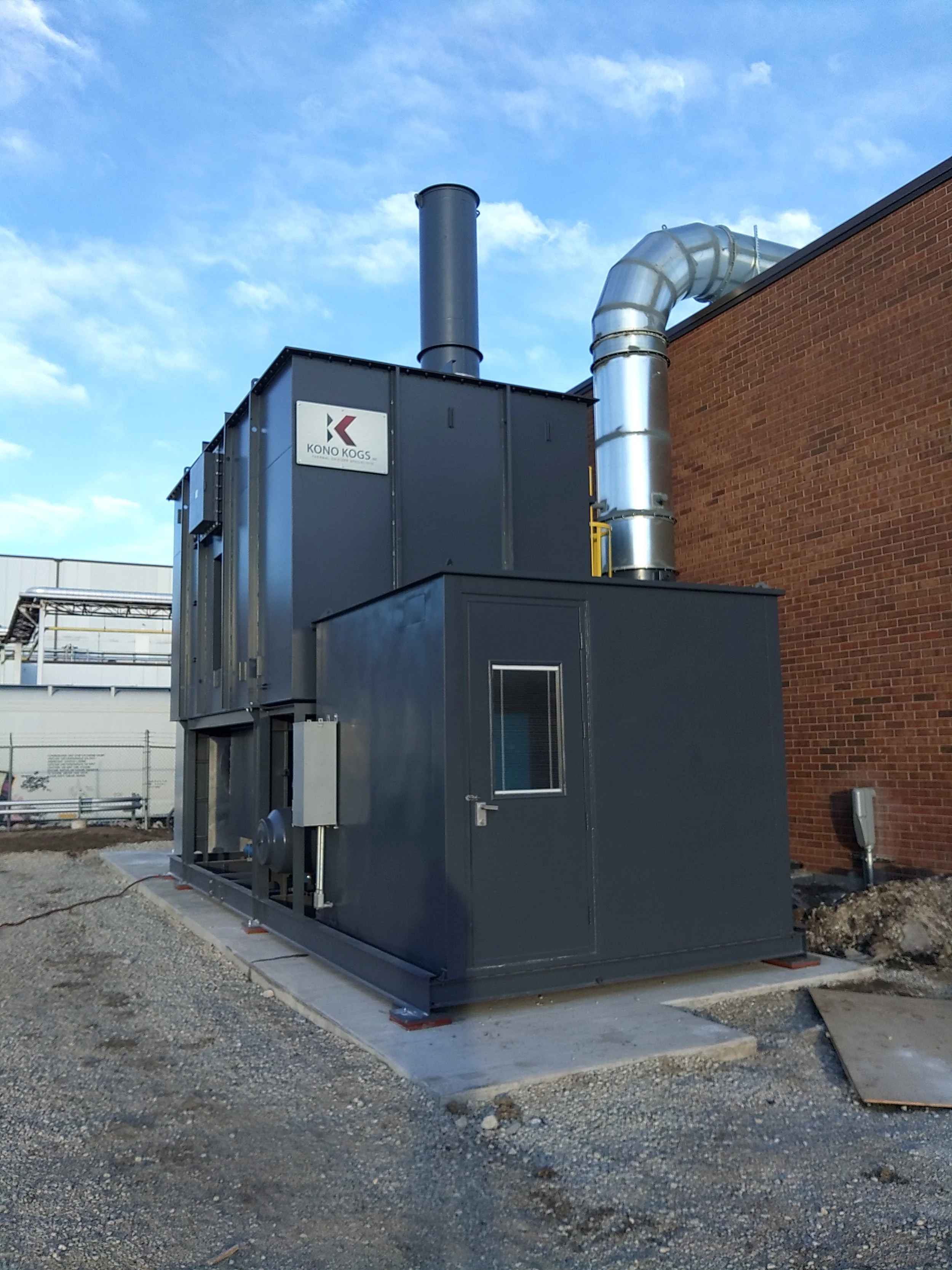 Industrial HVAC system with ductwork and machinery outside near a brick building under a partly cloudy sky.