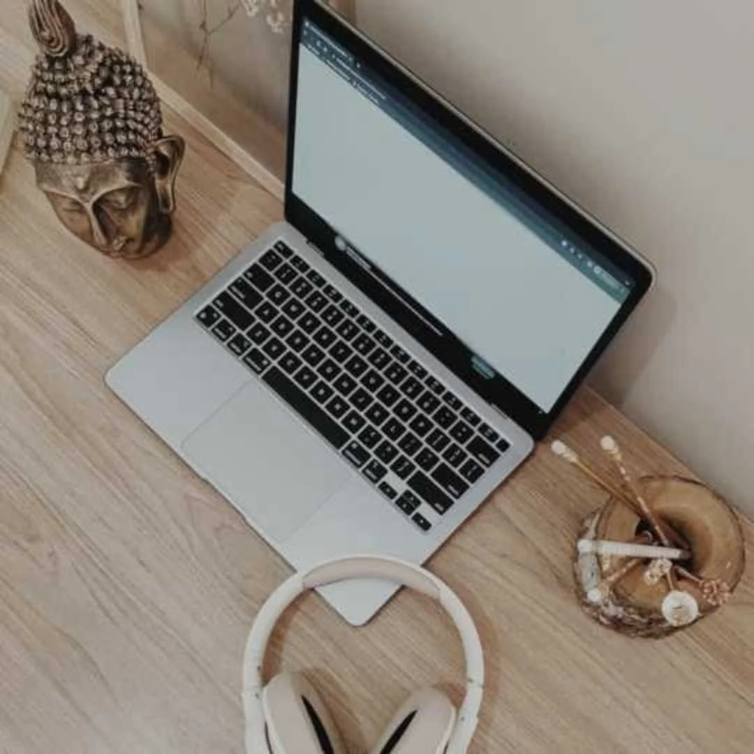 Laptop and headphones arranged on a desk beside a small Buddha statue.