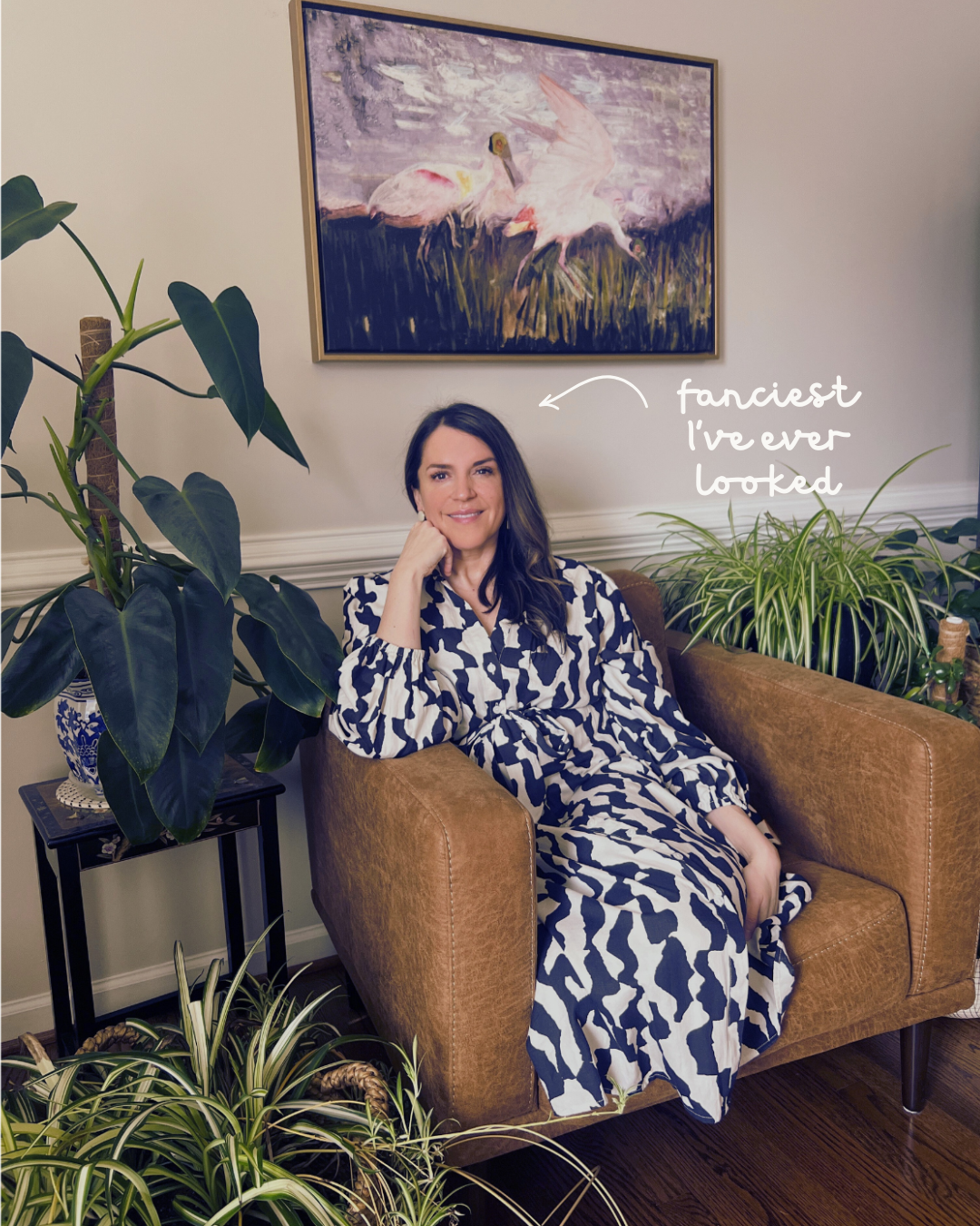 Mel Rolfes seated in an armchair surrounded by plants, with a handwritten arrow pointing to her that reads, “fanciest I’ve ever looked.”