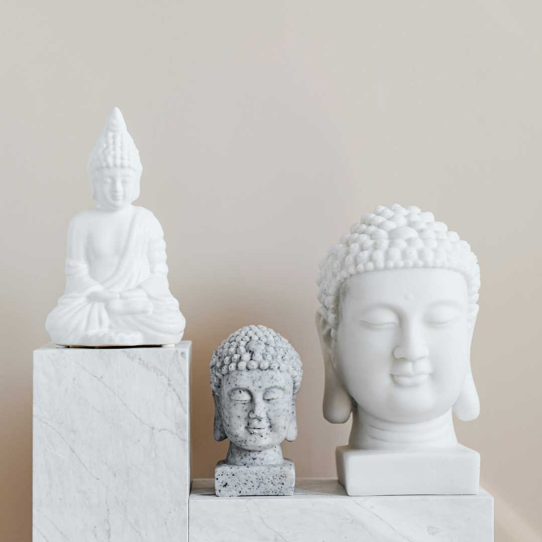 Three neutral-toned Buddha statues arranged on marble pedestals.