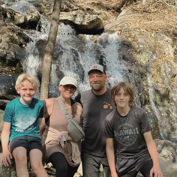 Mel Rolfes with her partner and his two sons standing together in front of a waterfall.