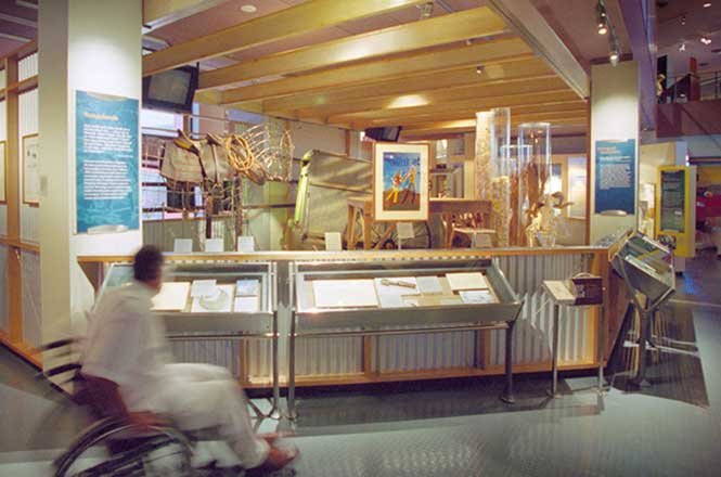 At the National Museum of Australia, a Museum exhibit with display cases and informational panels, person in wheelchair in foreground