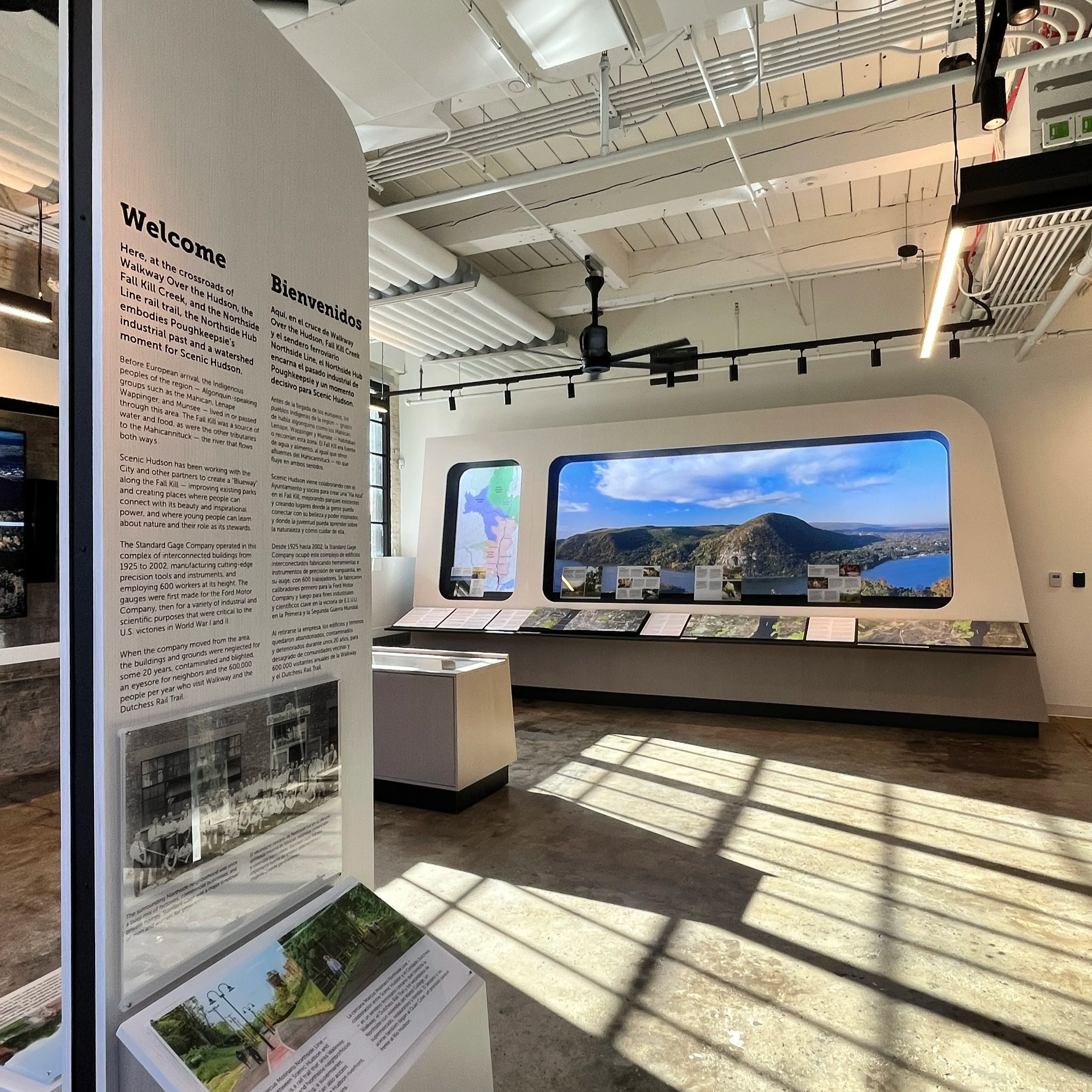 Museum exhibit with historical information panels, photographs, and a large landscape photograph of mountains and blue sky.