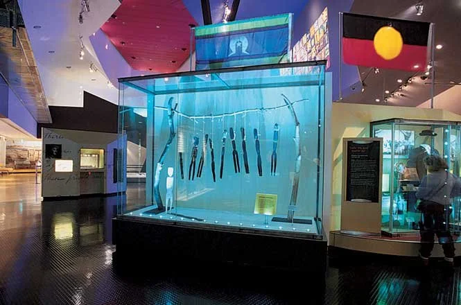 Display case with various ancient tools and artifacts in a museum, with informational signs and flags nearby.