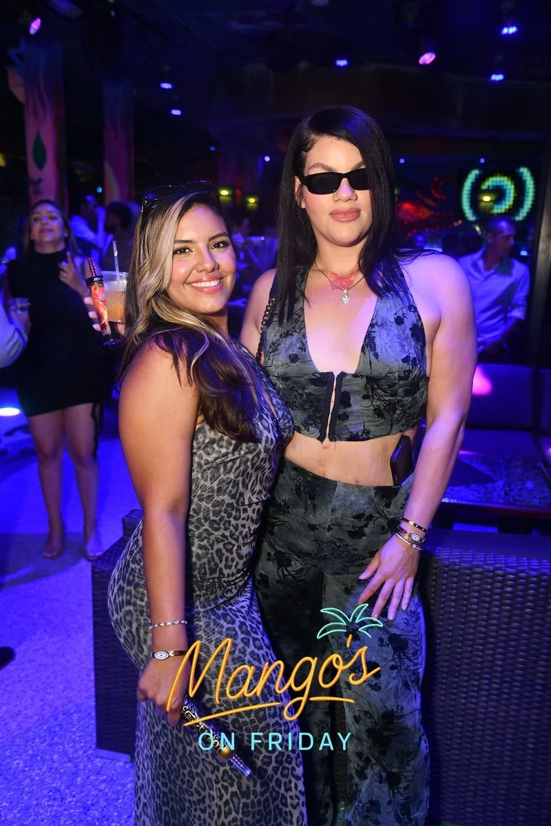 Two women in a nightclub with colorful lights, one wearing a leopard print dress and the other in a black and gray floral outfit with sunglasses. A woman in the background is holding a drink. The text 'Mango's On Friday' is overlaid at the bottom of 