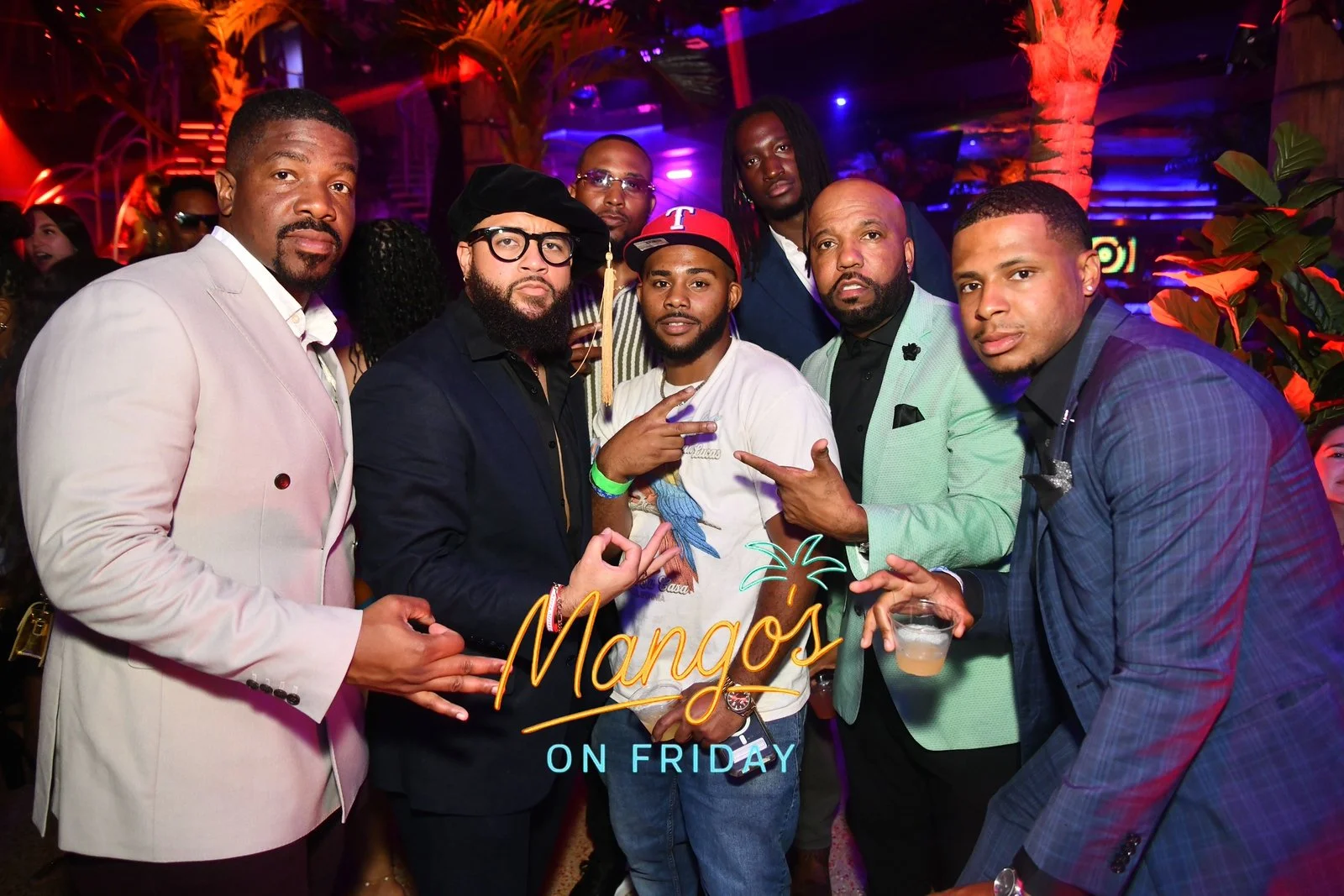 Group of men at a night event under colorful lighting, with a neon sign reading 'Mango's on Friday' in the foreground.