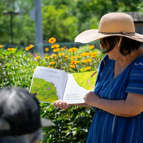 Instructor reading a children’s book among flowers in a community garden