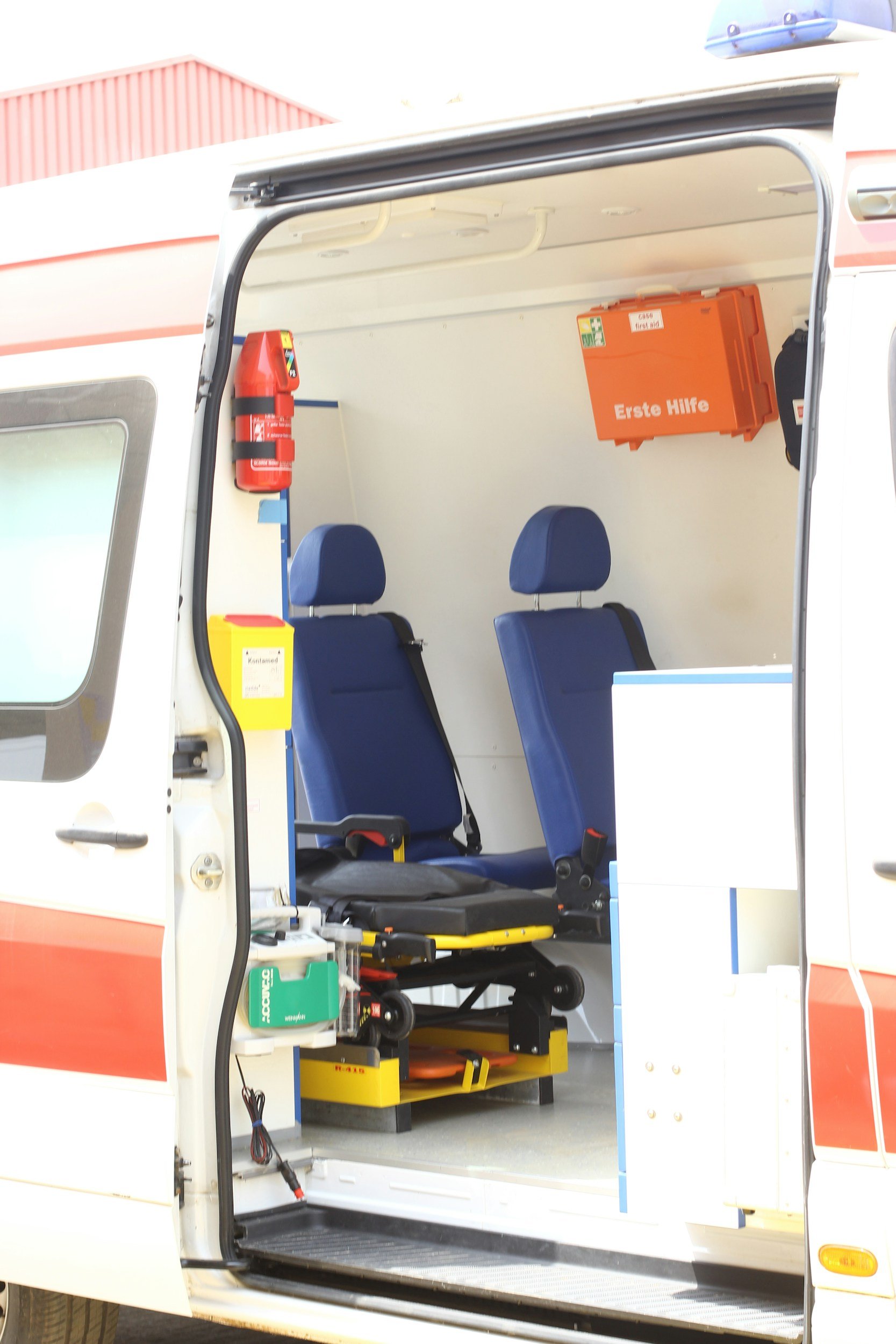 Innenraum eines Rettungswagens mit blauen Sitzen, medizinischen Notfallausrüstungen und einem Erste-Hilfe-Koffer