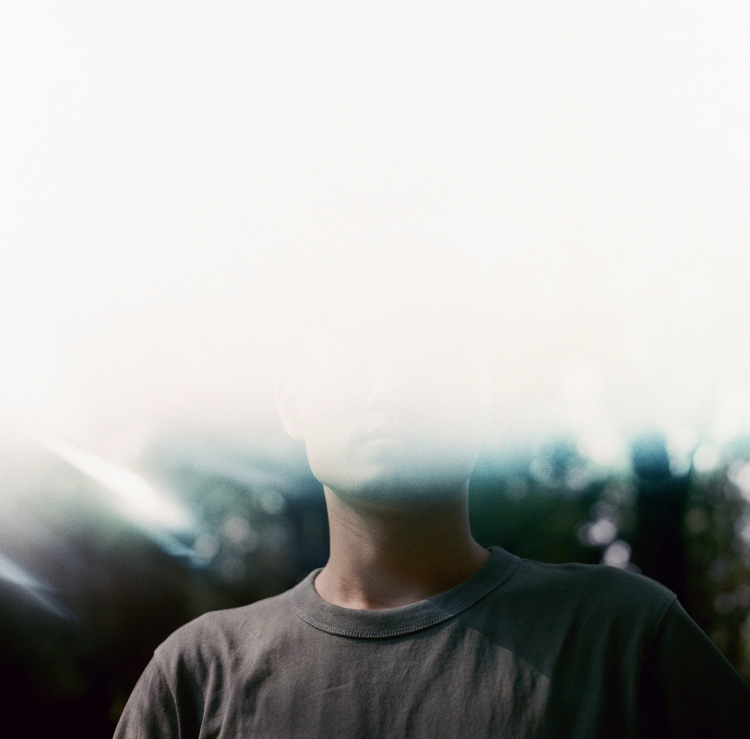 Porträt eines jungen Mannes, der einen grauen Pullover trägt, mit dunkelblonden, lockigen Haaren, vor einem unscharfen grünen Hintergrund.