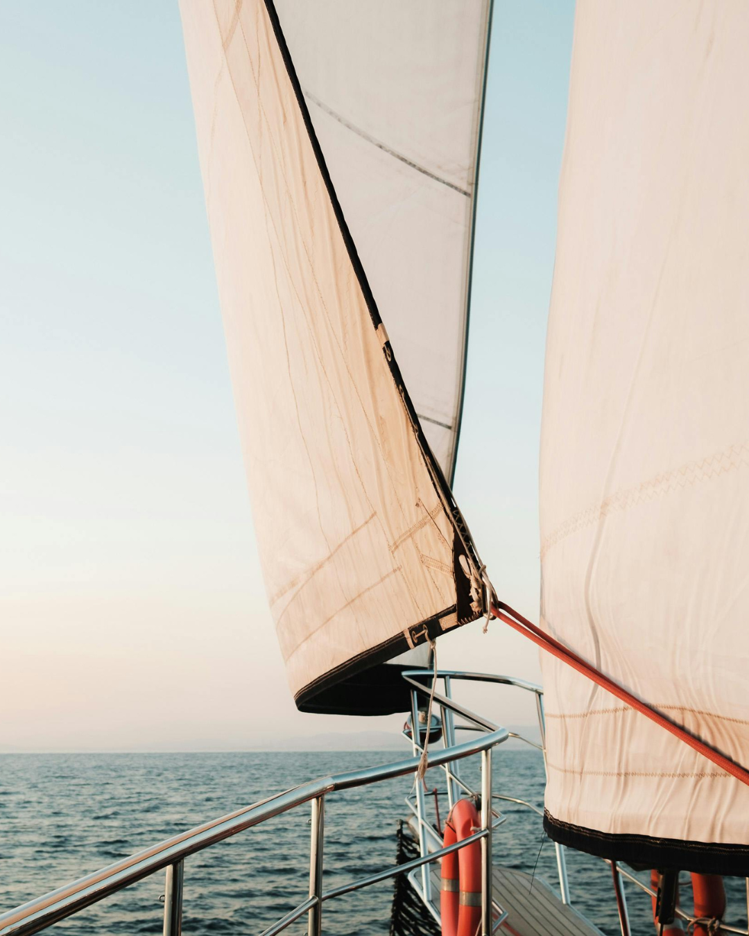 Close-up of a sailboat's sail and safety railing at sunset
