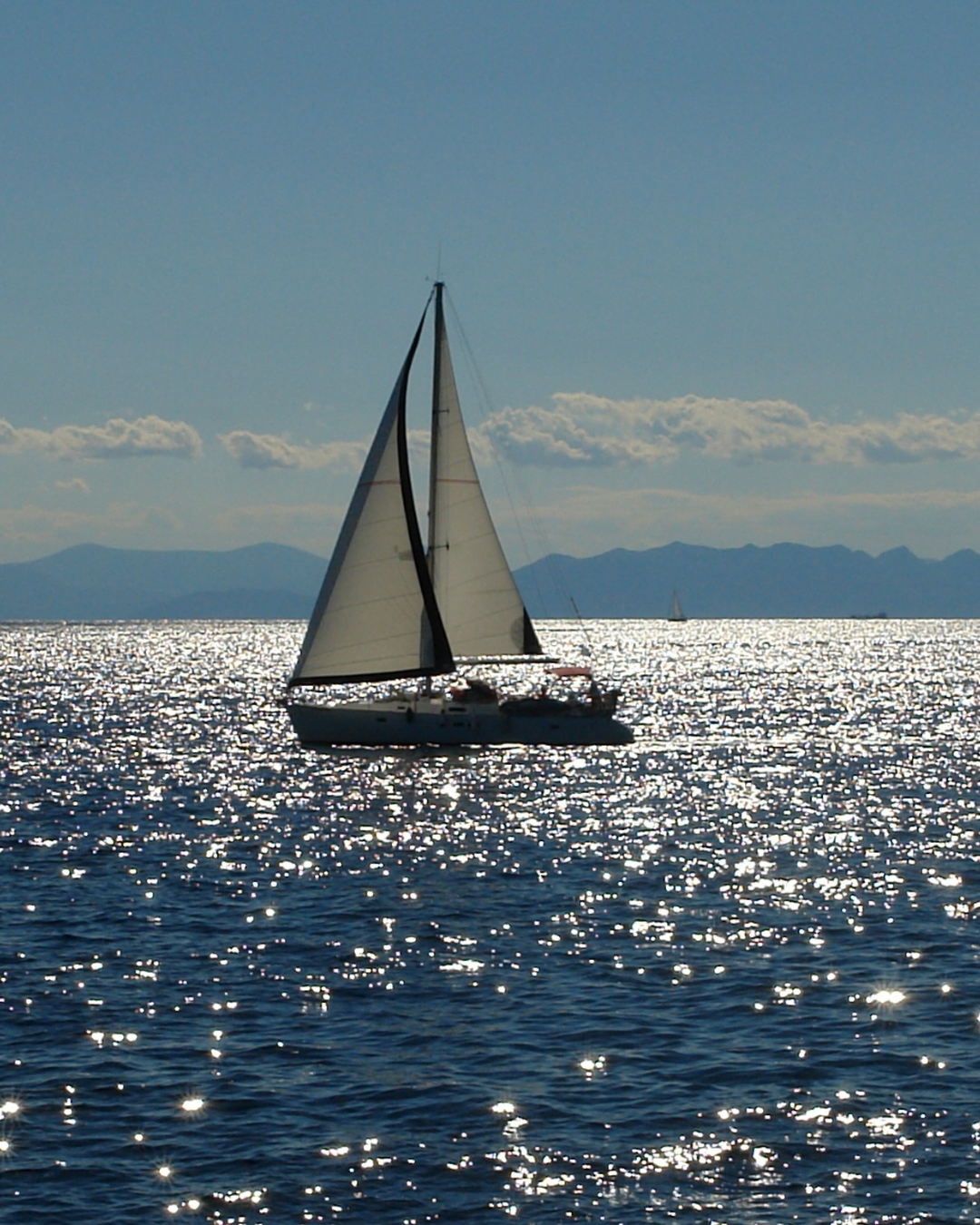 Sailboat gliding across sunlit water with mountains in the background