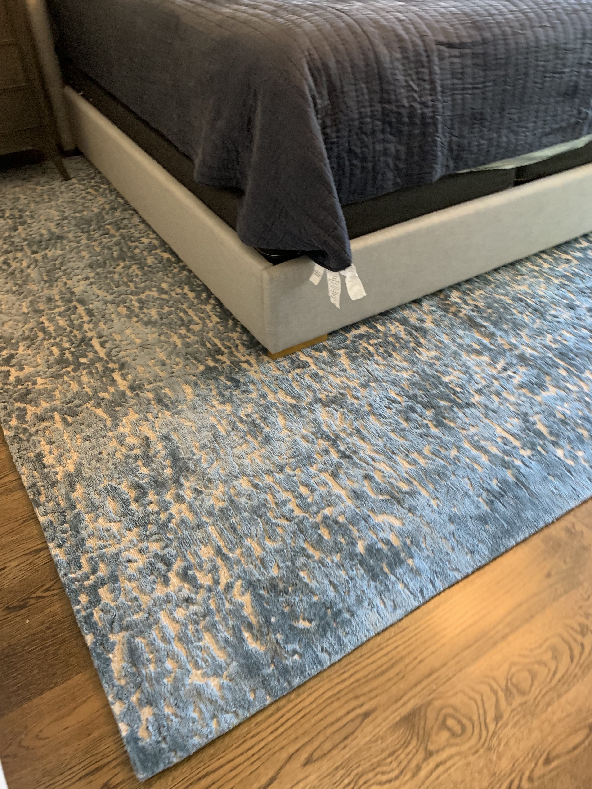 Close-up of a gray upholstered sofa with a dark throw blanket and patterned blue area rug on a hardwood floor