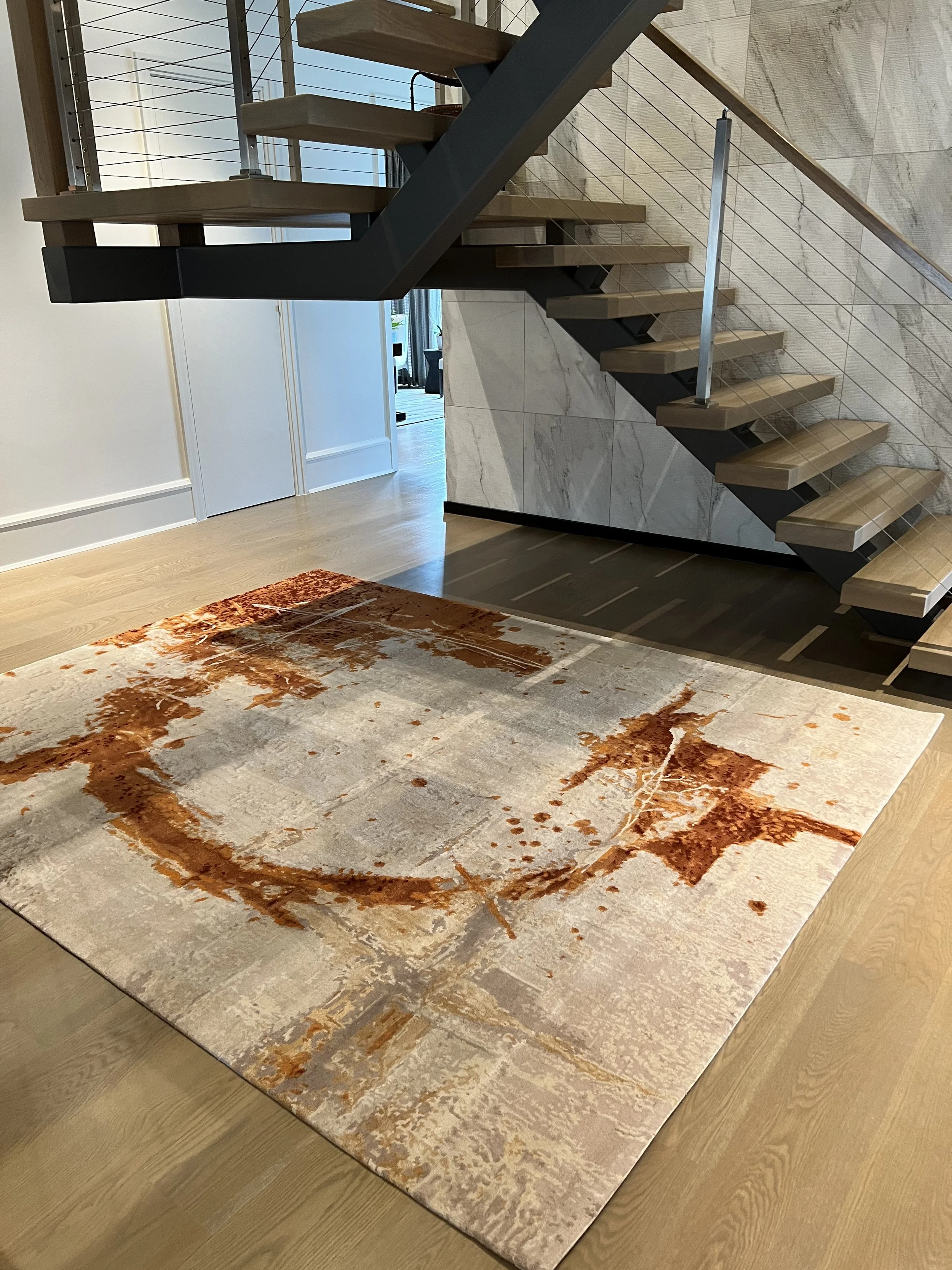 Modern floating wooden staircase with black supports and cable railing above an abstract gray and rust area rug