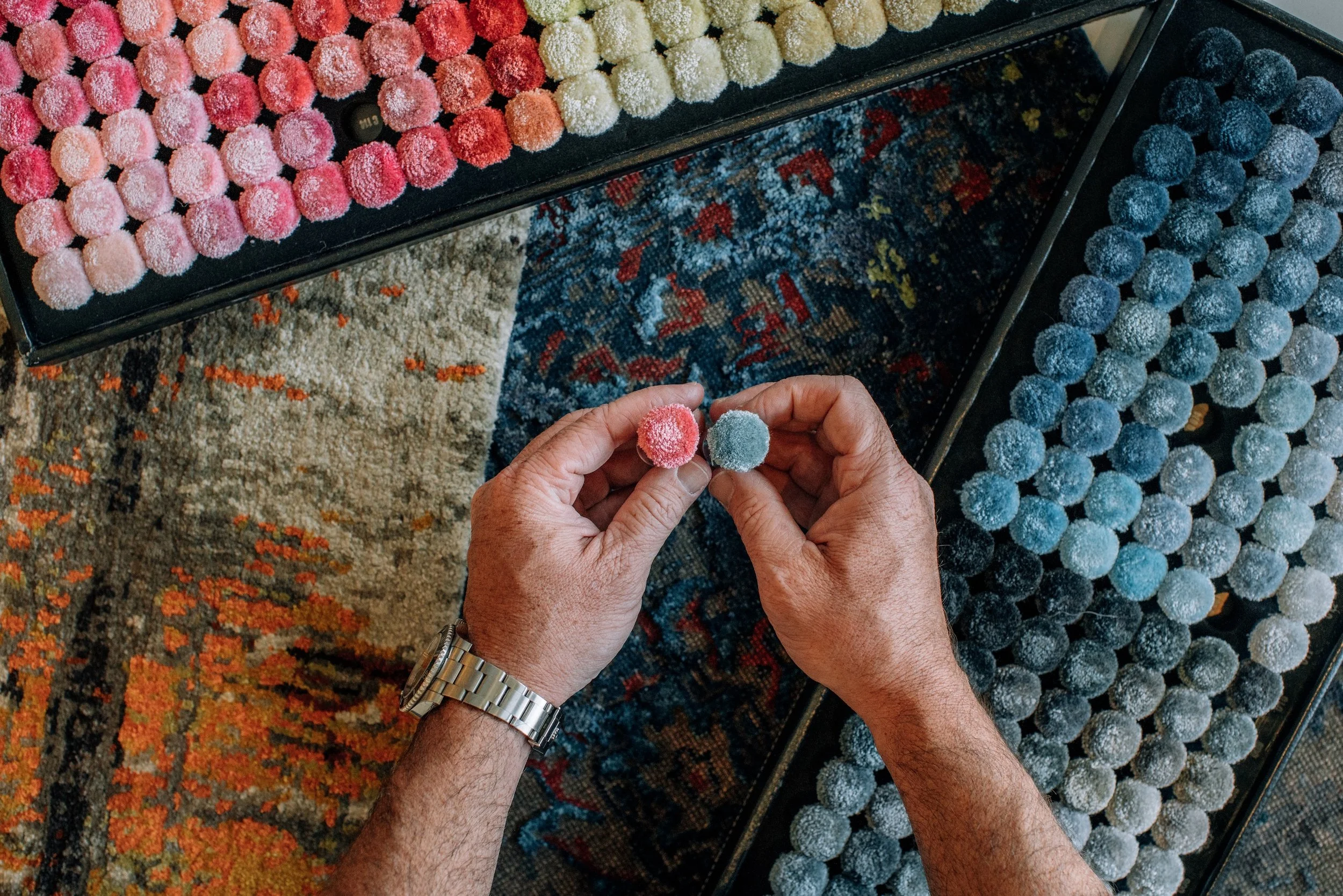 Hands comparing pink and blue tufted carpet samples among colorful rug swatches