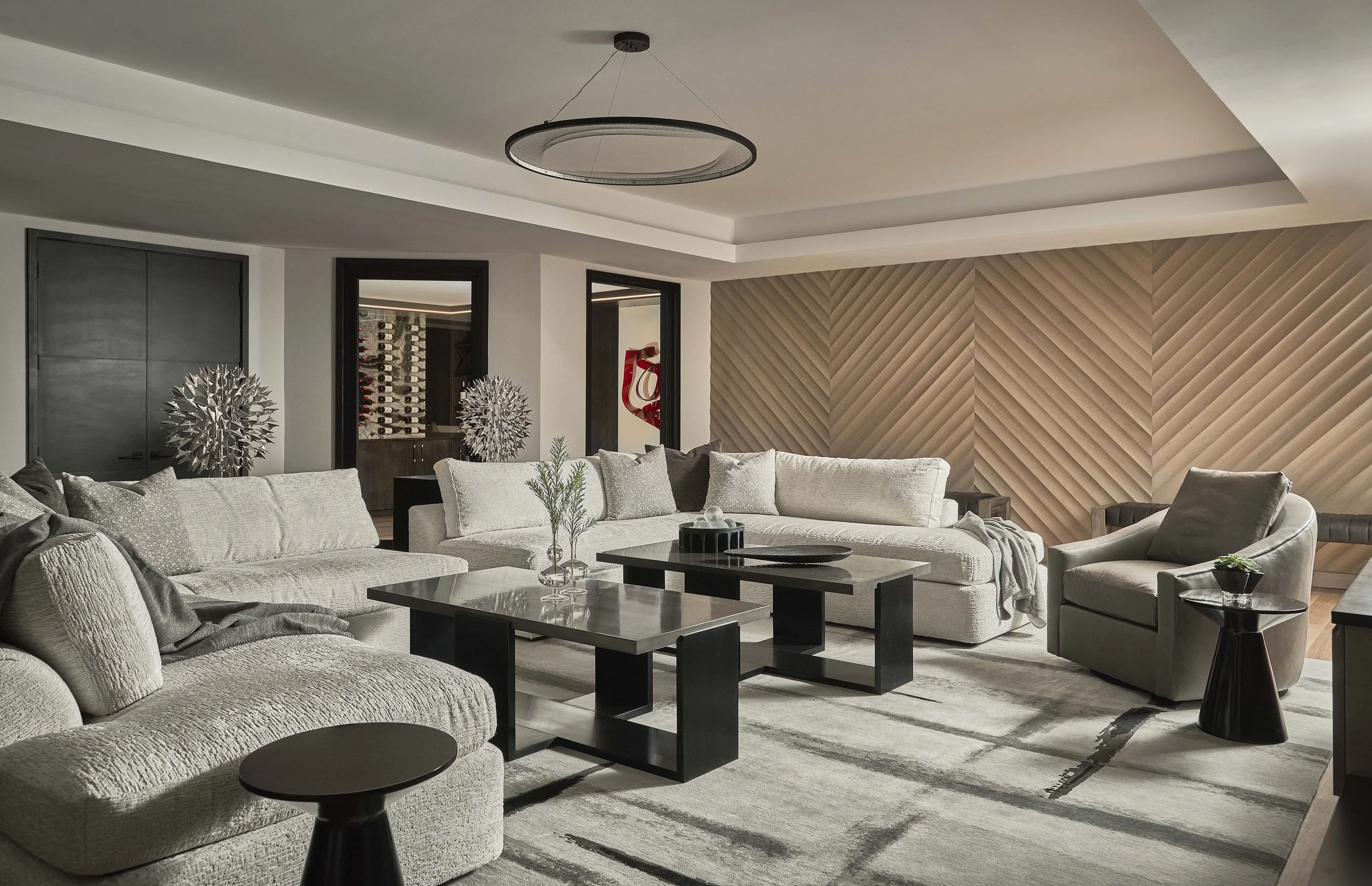 Modern luxury living room with gray sofas, black coffee tables, geometric wood accent wall, and wine display