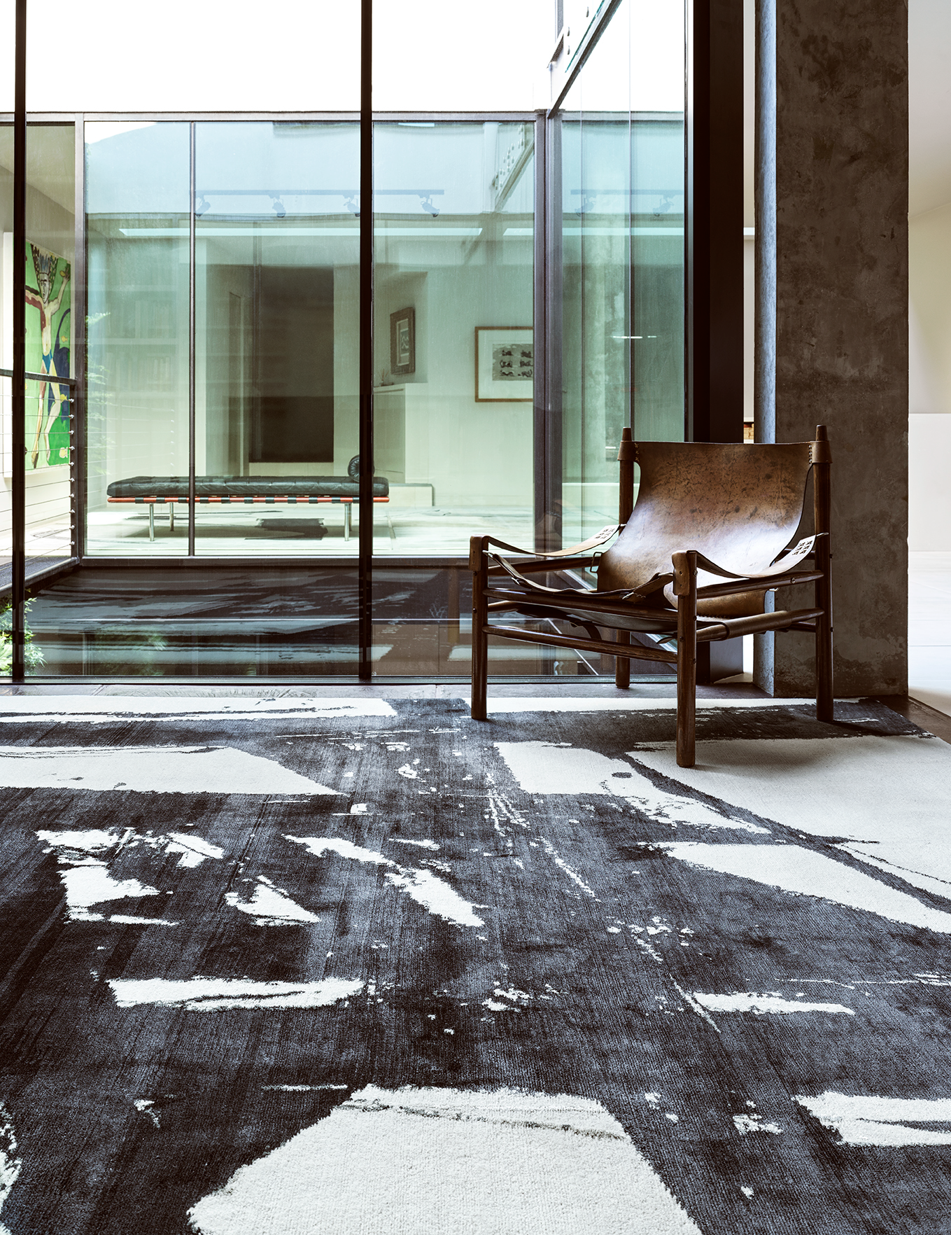 Modern interior with a leather sling chair, glass wall, artwork, and abstract black-and-white area rug