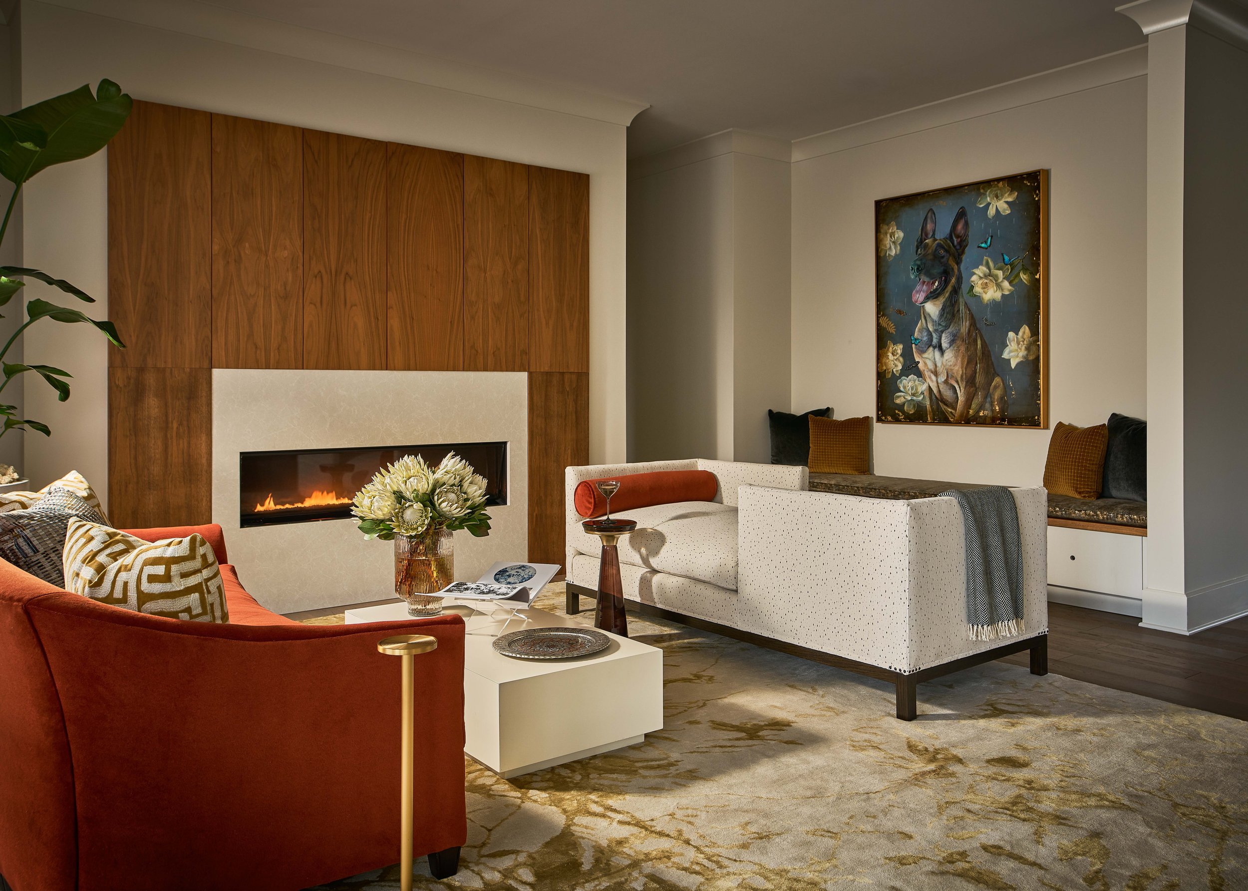 Elegant modern living room with a fireplace, wood-paneled accent wall, colorful furniture, floral centerpiece, and German Shepherd artwork