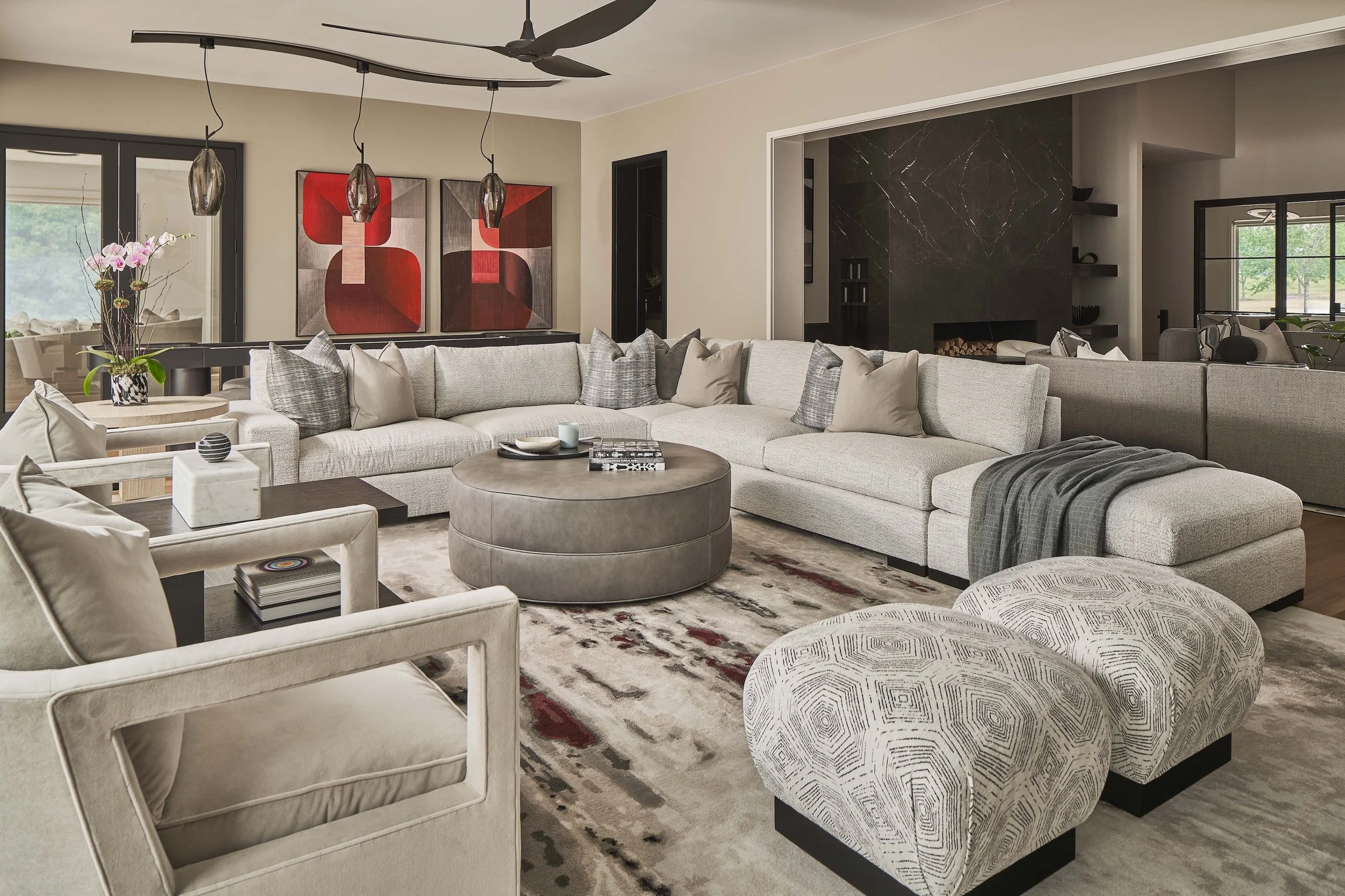 Modern luxury living room with a large sectional sofa, round coffee table, patterned ottomans, abstract artwork, pendant lights, and black marble fireplace