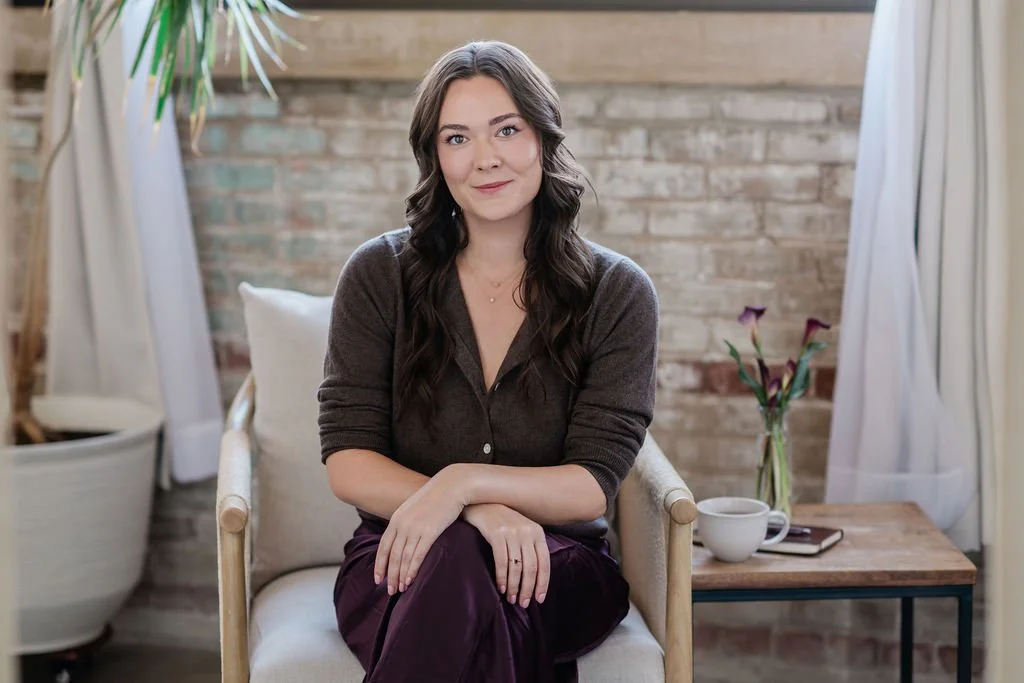 Woman with long dark hair sitting in an armchair in a cozy brick-walled room