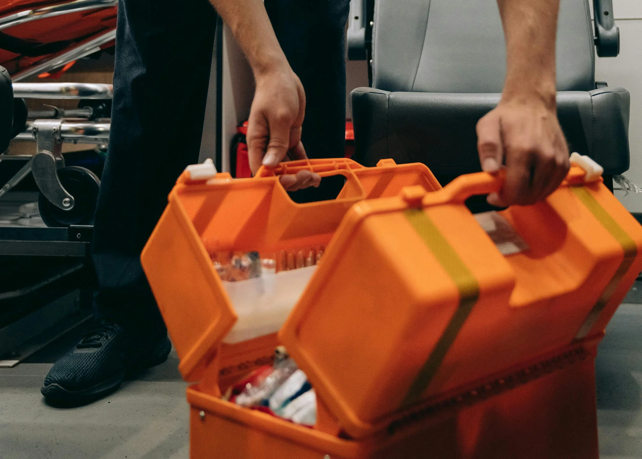 Close-up of hands holding an orange plastic toolbox filled with various tools and screws.