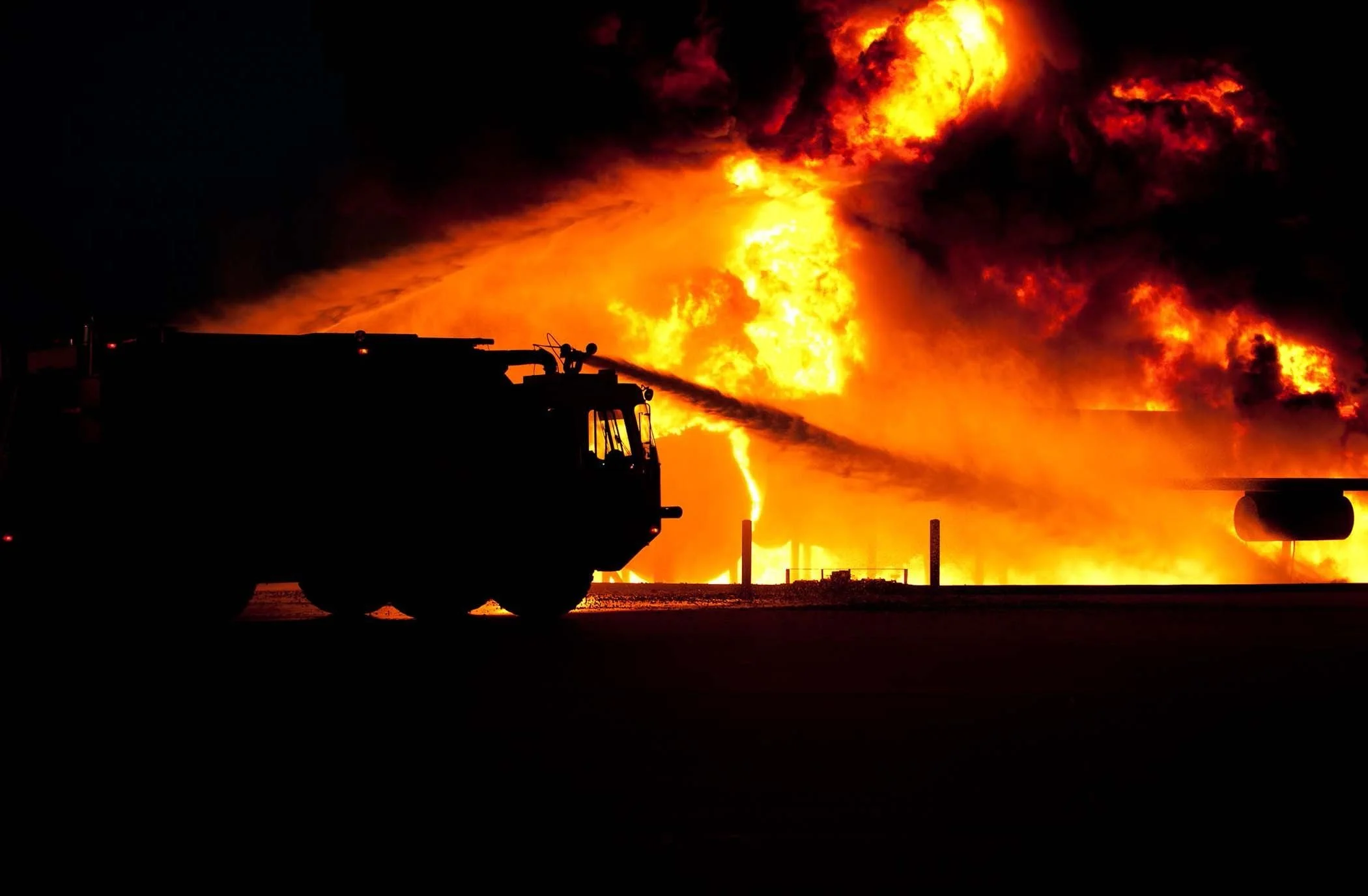 A fire truck spraying water on a large fire with flames and smoke in the background.
