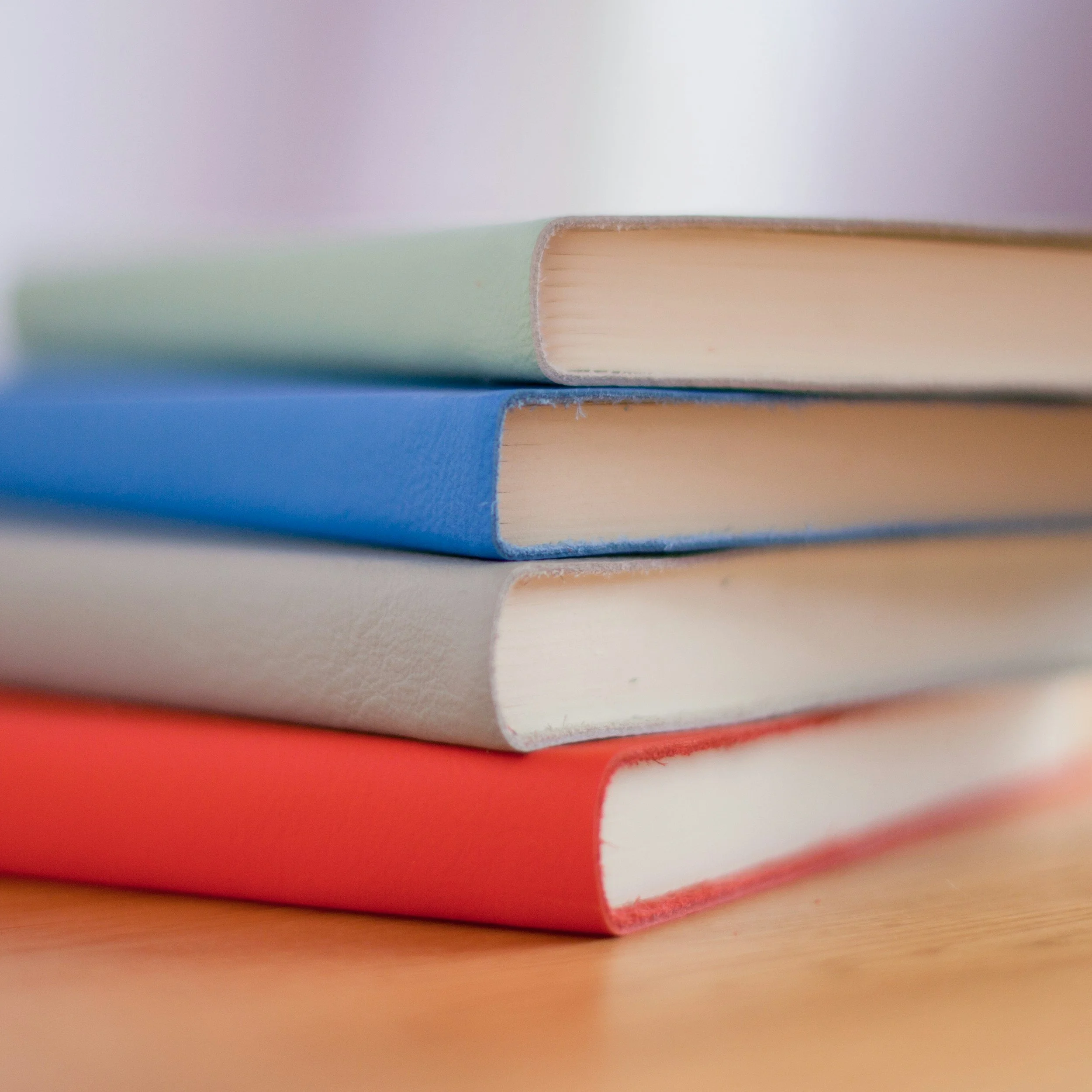 Close-up of a stack of colorful books with the focus on the spines, featuring shades of red, white, green, and blue.