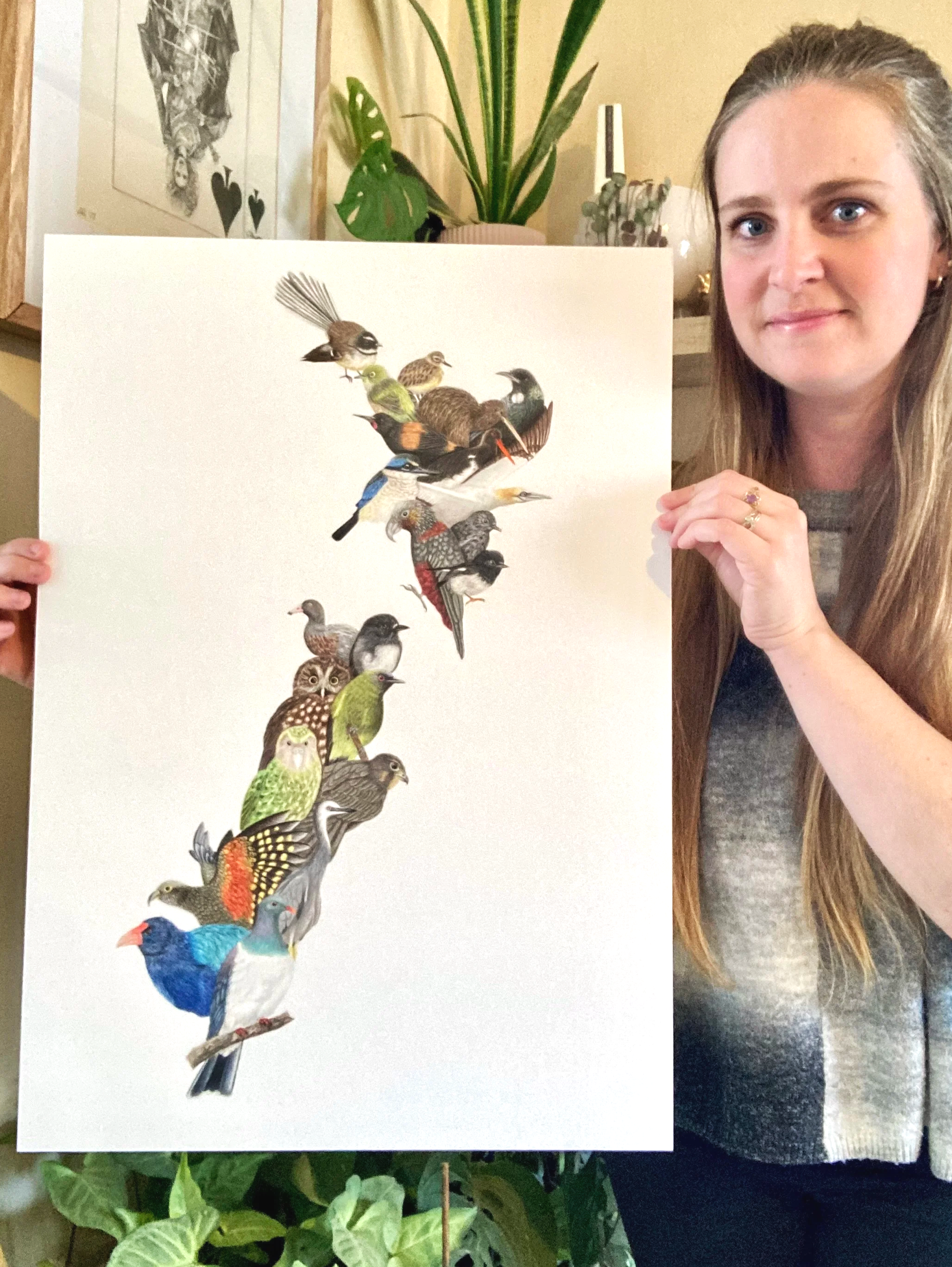 A woman holding a poster featuring various colorful birds, with plants in the background.