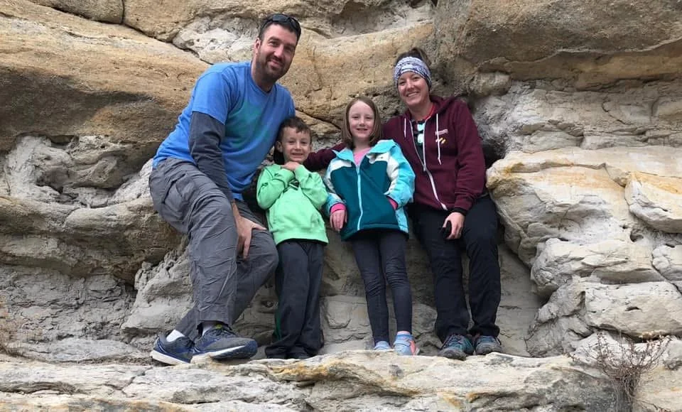 A family of four posing in front of a rocky formation during an outdoor hike.