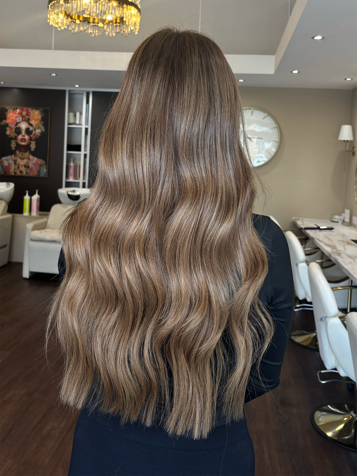 Back view of a woman with long, wavy, light brown hair in a salon