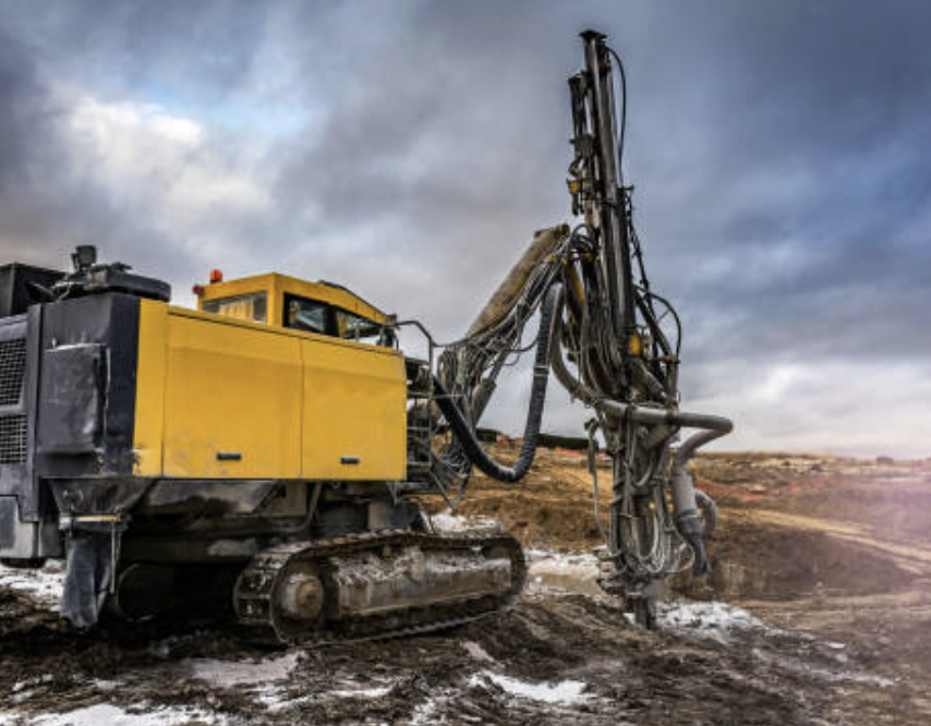 Heavy construction drill with yellow body and black tracks operating on muddy terrain under cloudy sky.