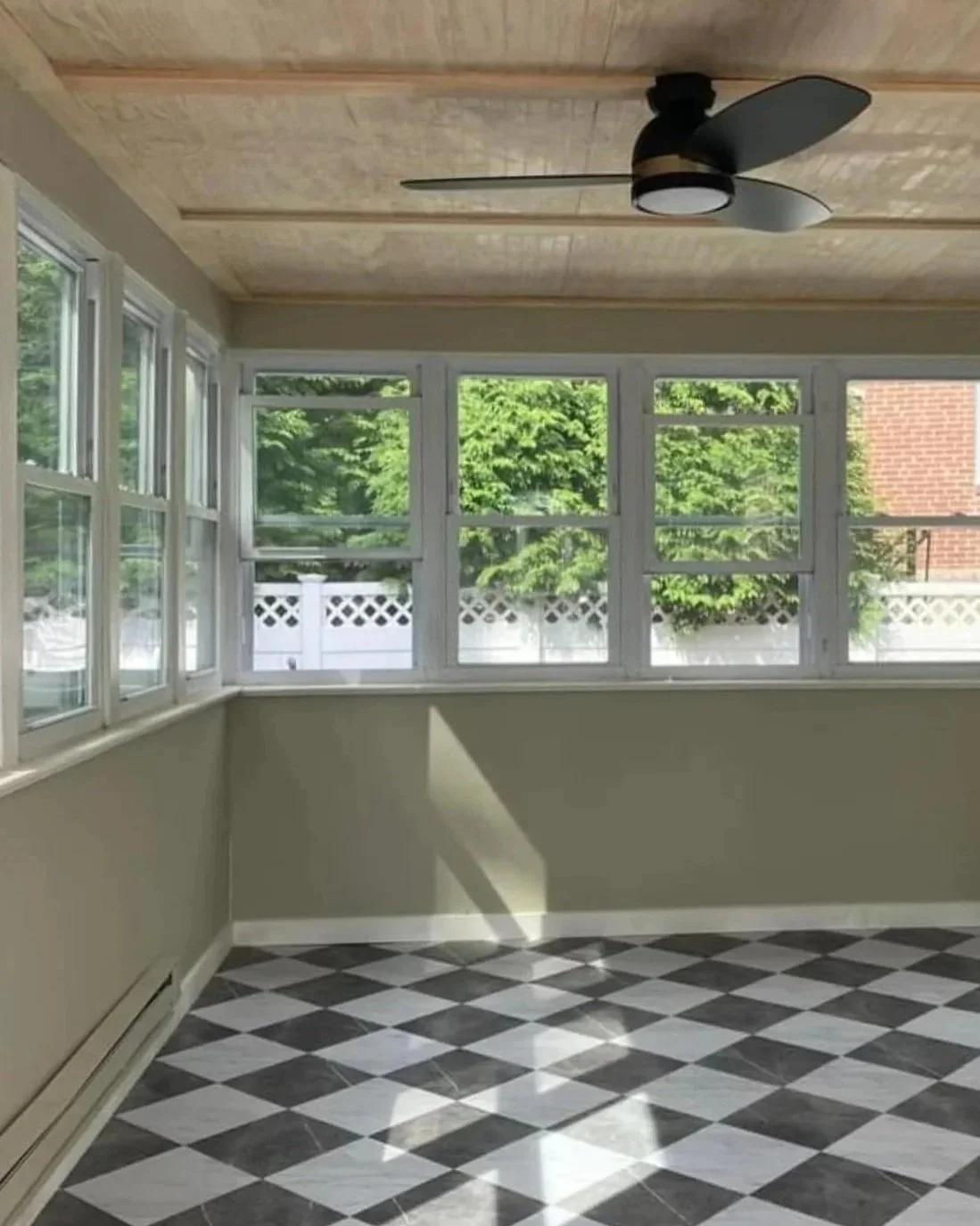 Empty room with multiple windows, a black ceiling fan, green trees outside, and a black and white checkered floor.