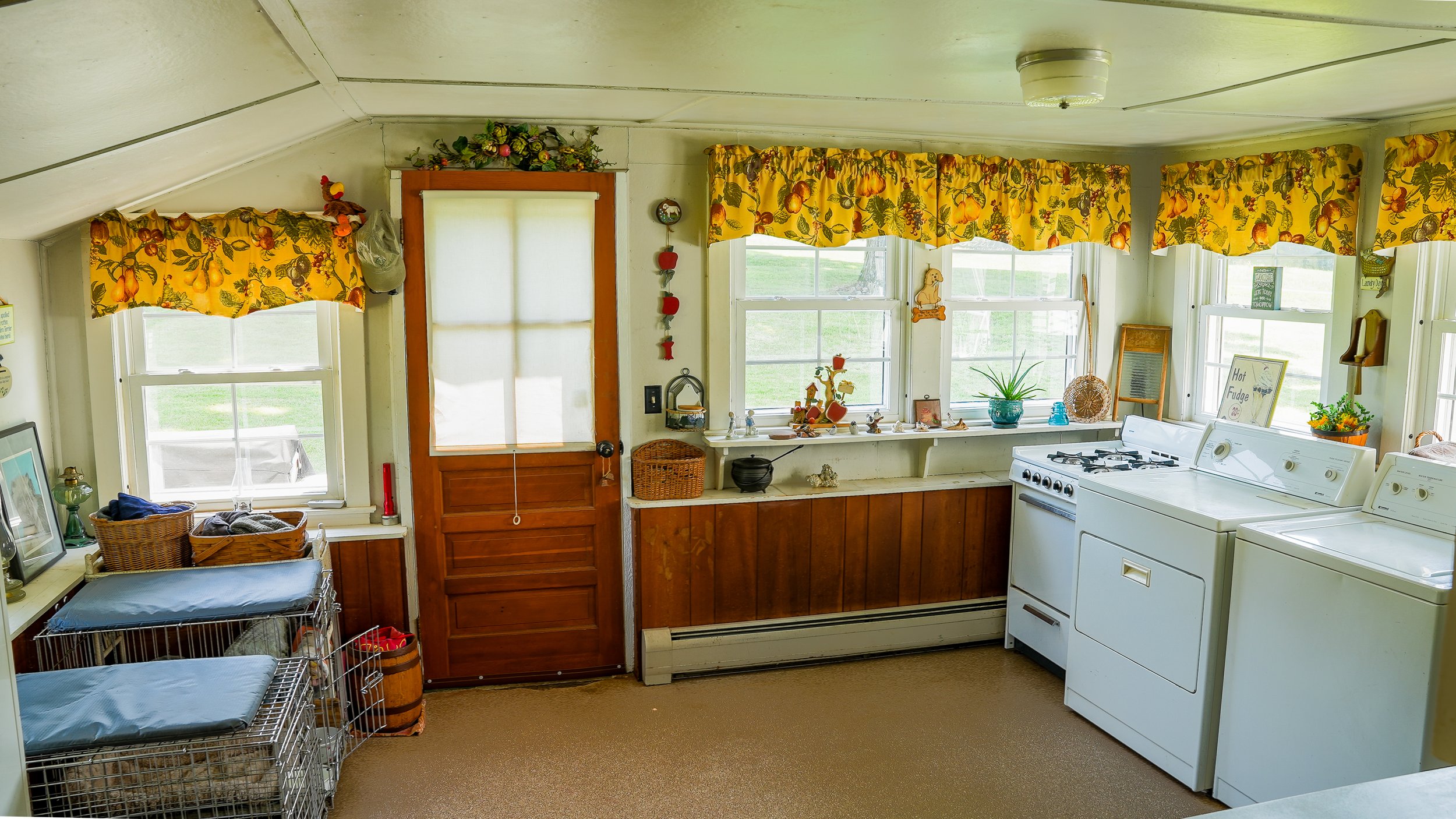 Bright kitchen with yellow floral curtains, white appliances, and wooden cabinets, decorated with plants and small decorative items.
