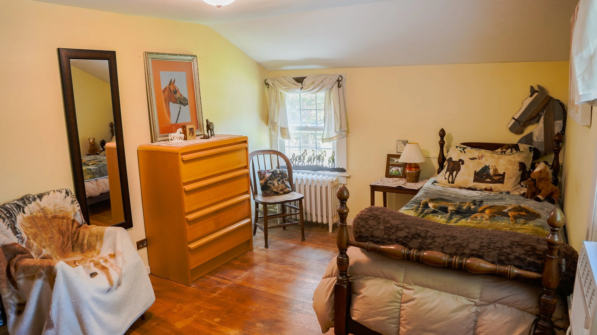 A cozy bedroom decorated with horse-themed items, featuring a window with horse silhouettes, a bed with horse-patterned bedding, a dresser, mirror, and various horse figurines and artwork.