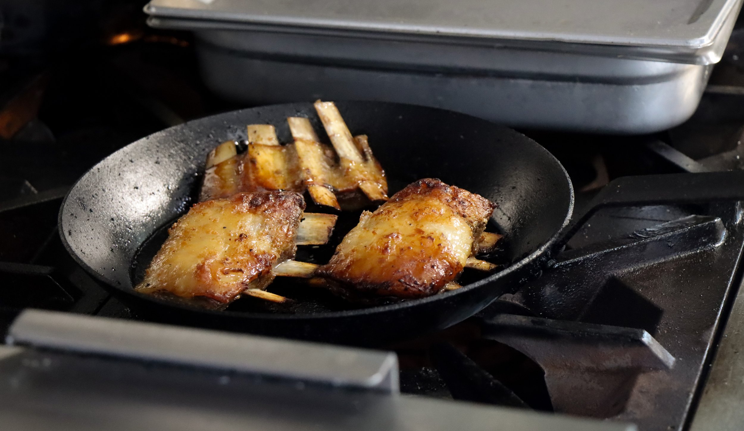 Frying pork ribs on a black skillet with a rack of ribs in the background.