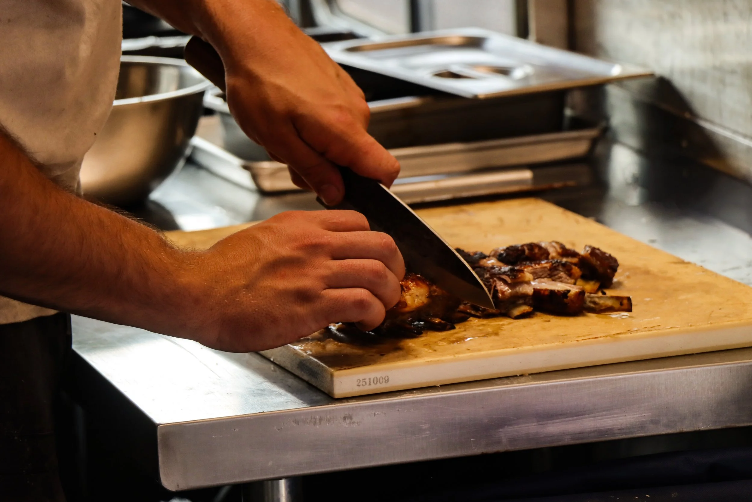 Person slicing cooked meat on a wooden cutting board in a professional kitchen.