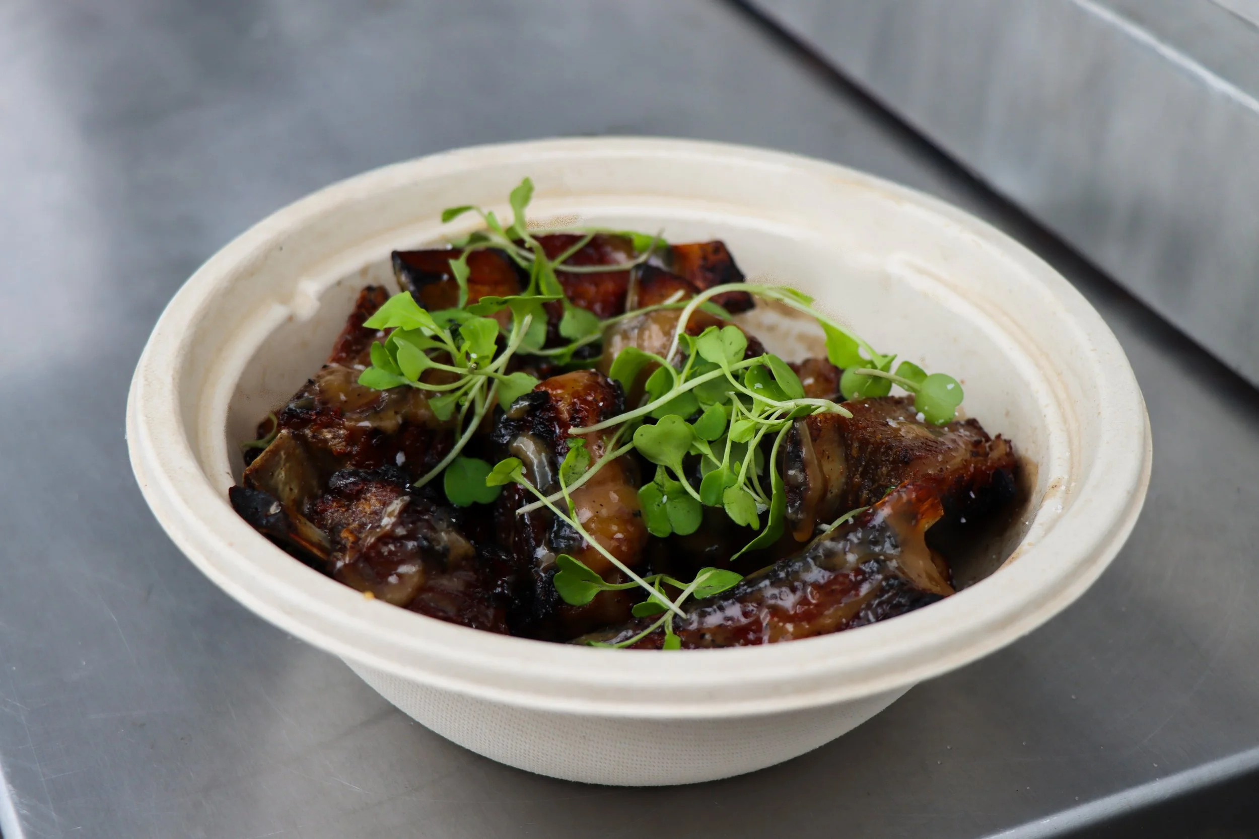 Bowl of grilled meat topped with microgreens on a gray surface.