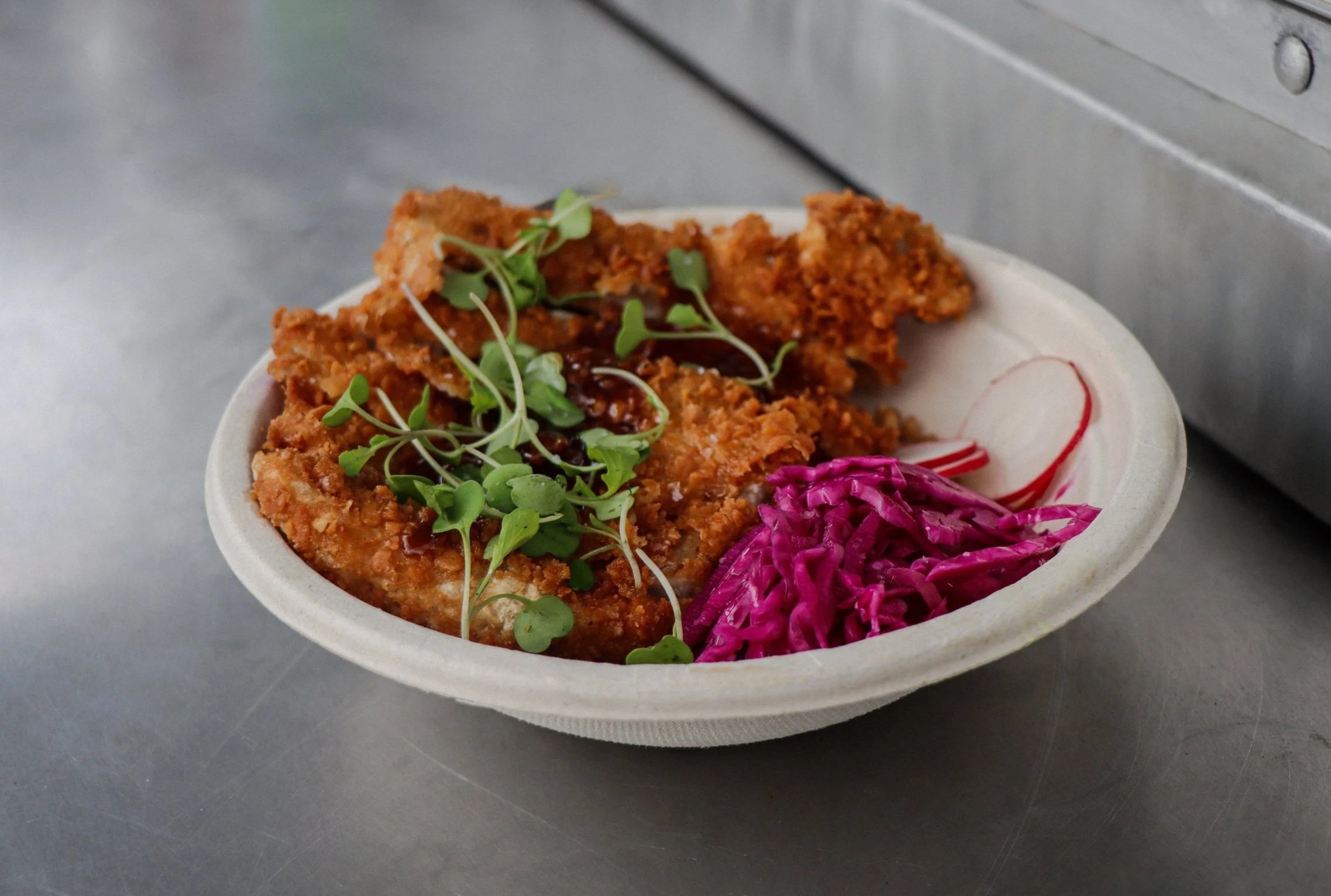 Deep-fried chicken strips garnished with microgreens, served alongside shredded purple cabbage and sliced radish in a white bowl.