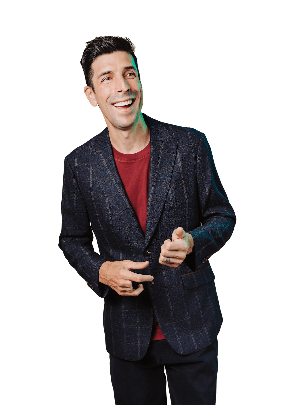 A man with dark hair wearing a plaid blazer and a red shirt, smiling and pointing with his right hand.