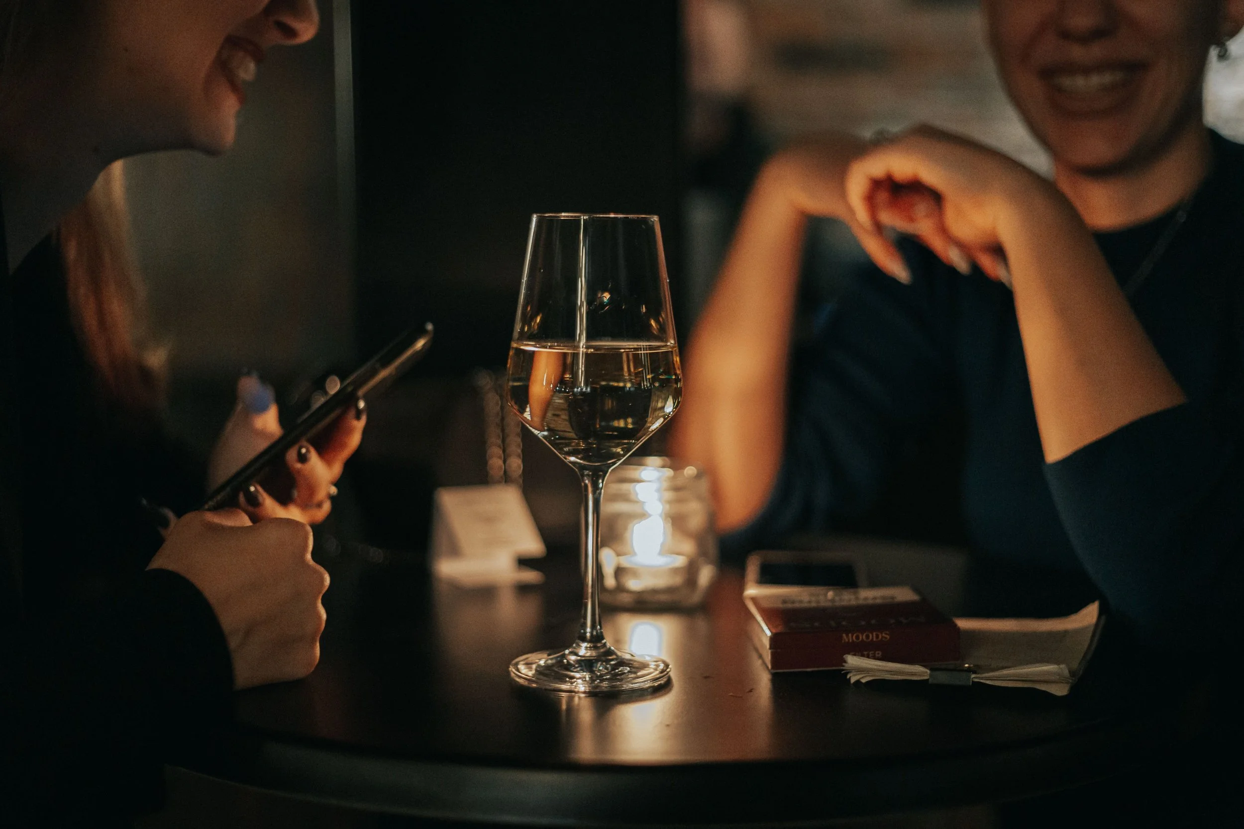 Two friends enjoying conversation over a glass of wine by candlelight, capturing the warm, welcoming atmosphere of Palace Wine Bar in downtown Rockford.