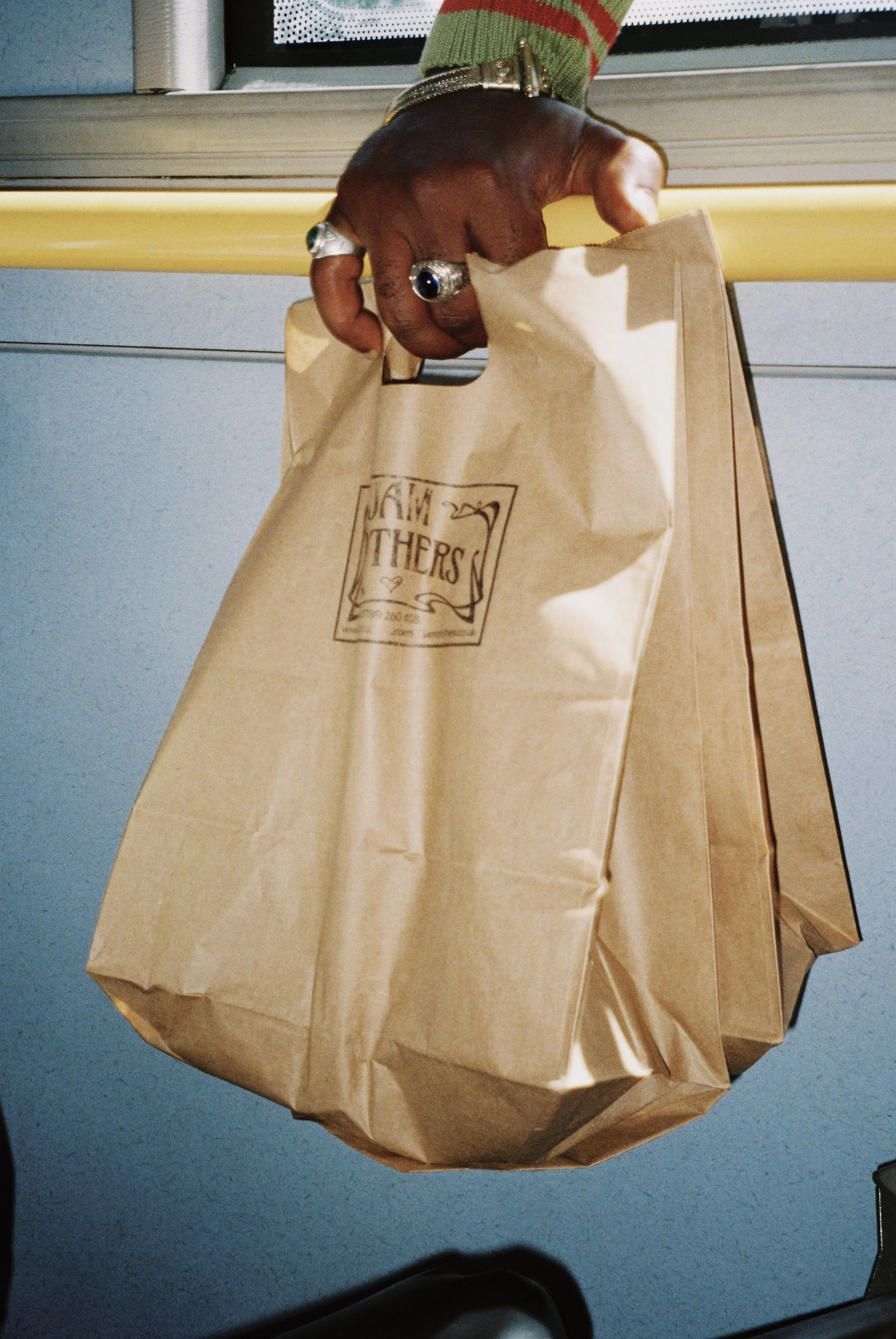 Hand with jewellery holding a paper bag of organic produce from organic farmers market on public transport in London, promoting sustainable food shopping.