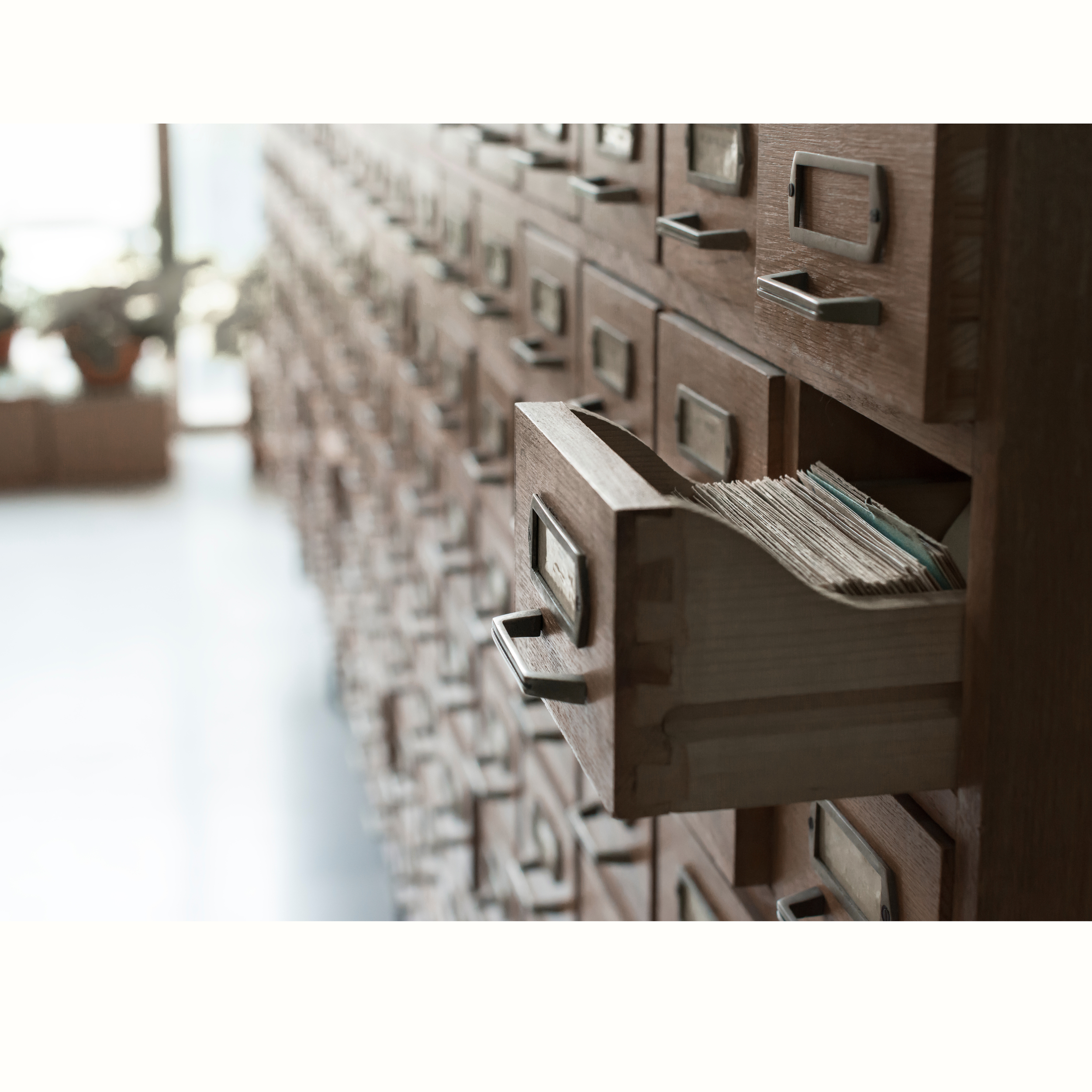 Close-up of a wooden filing cabinet with metal handles and label holders, partially open drawer with visible files or documents inside.