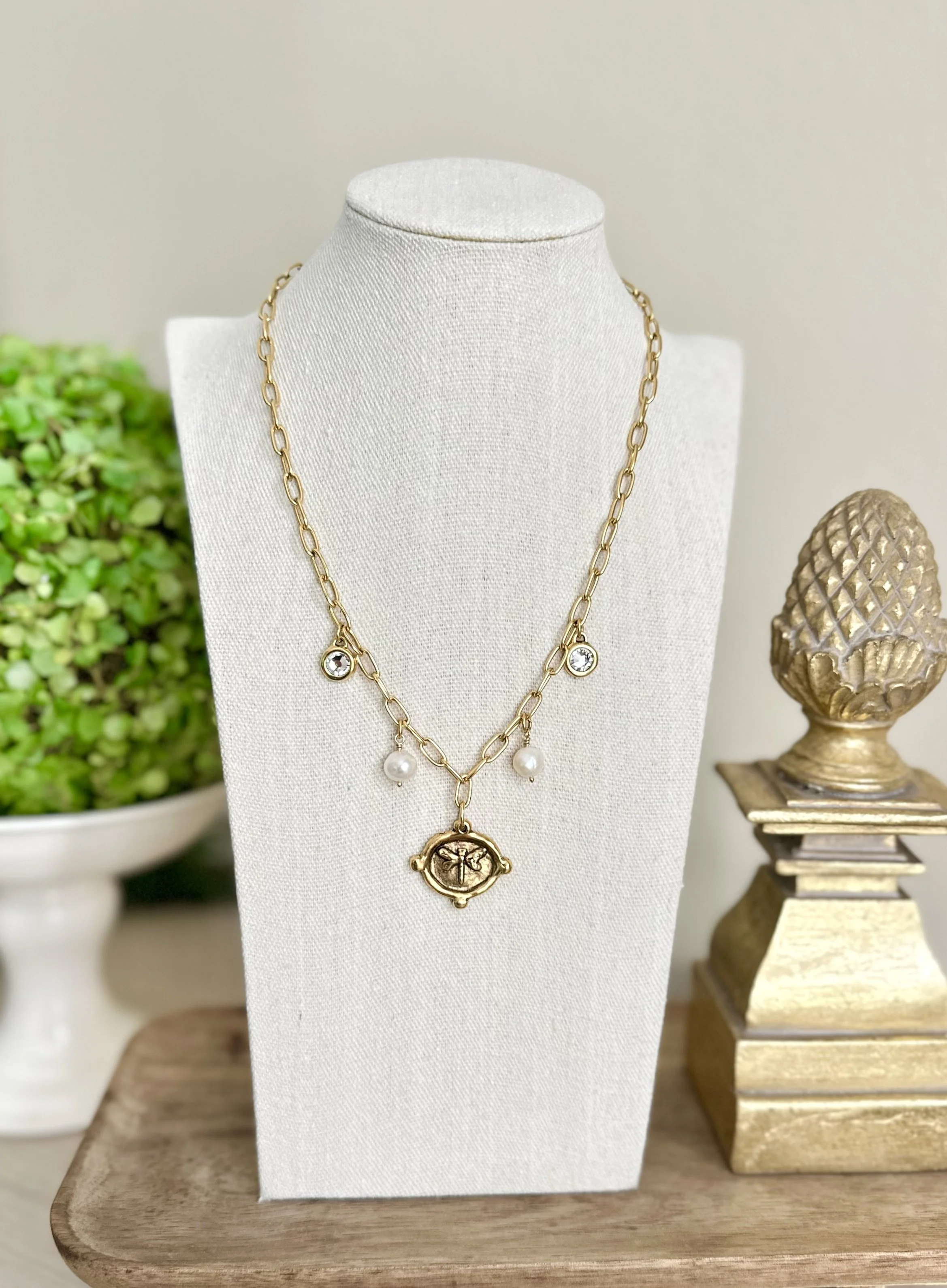 Gold chain necklace with clear gemstone accents and a dragonfly pendant, displayed on a white jewelry stand.