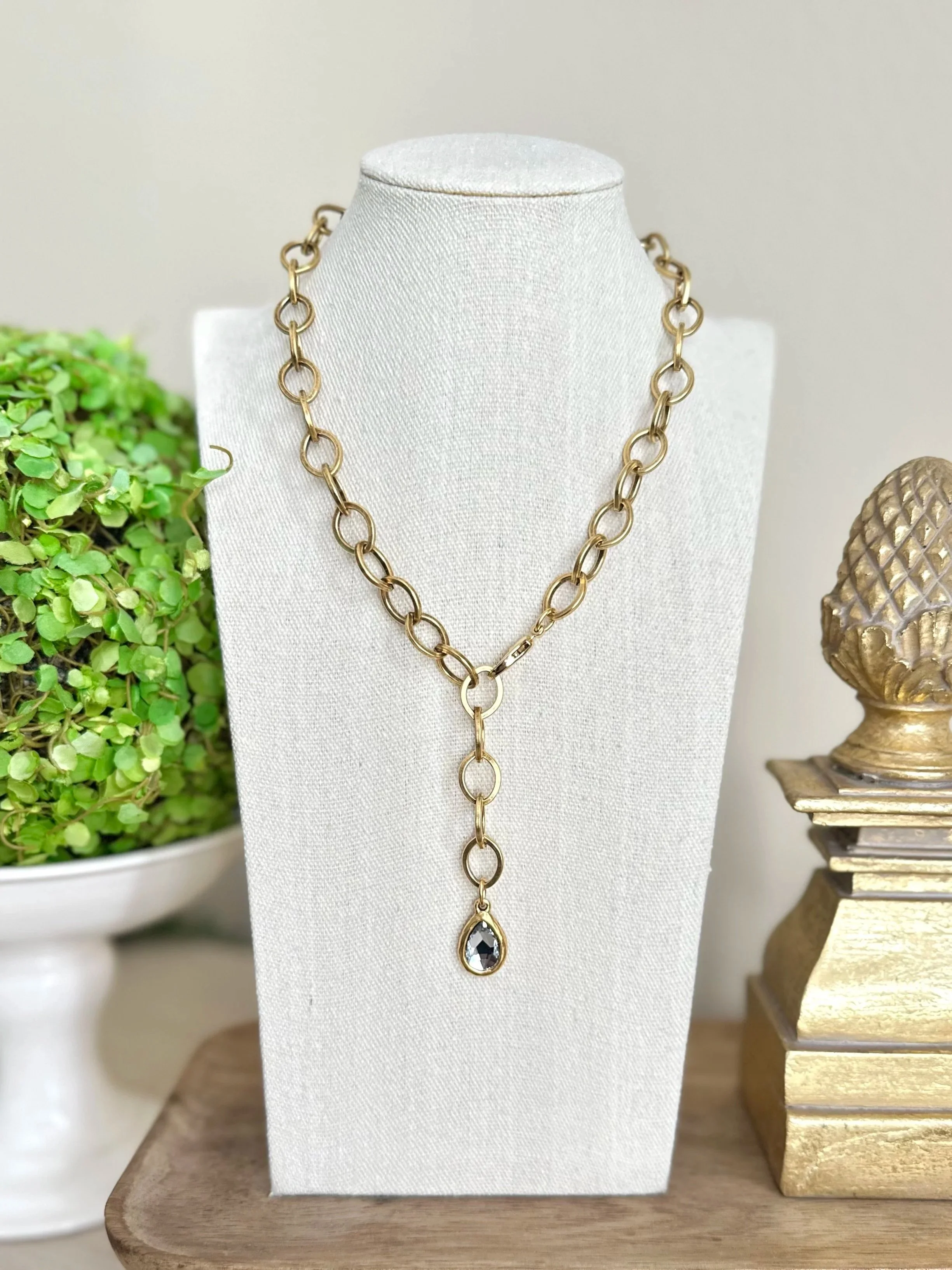 Gold chain necklace with large oval links and a black teardrop-shaped gemstone pendant, displayed on a white jewelry bust.