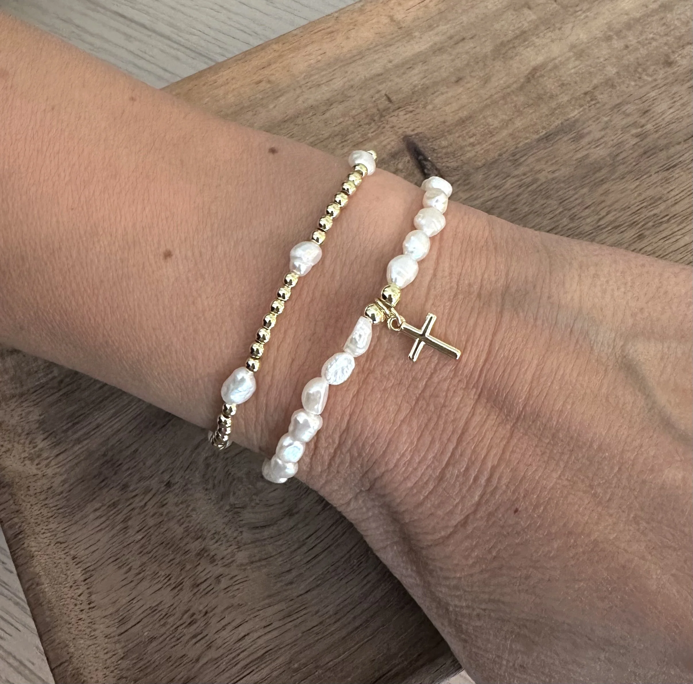Close-up photo of two bracelets: one with white beads and a cross charm, the other with gold-filled beads.