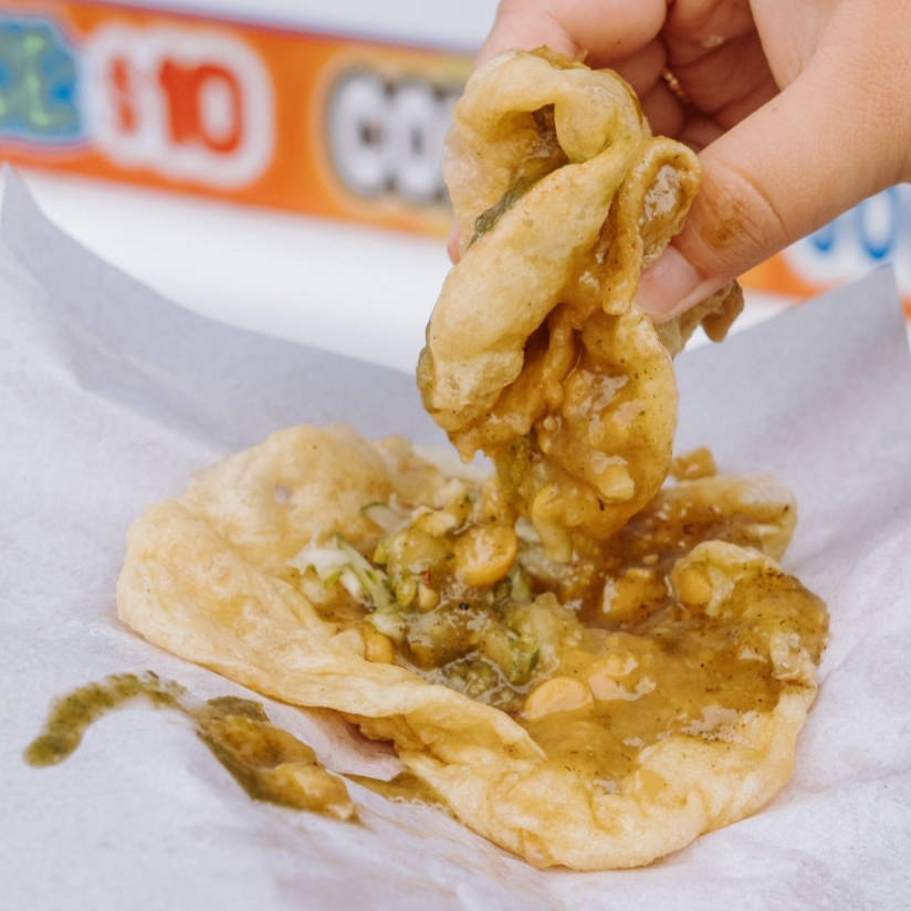 A hand dipping into a Trinidadian doubles, photographed by Brendan Miller of @fotodiaspora